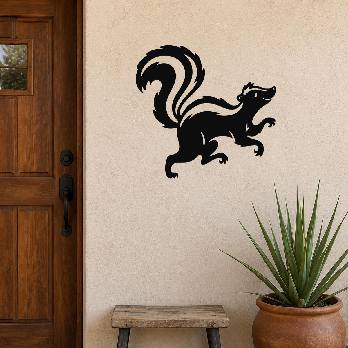 Black metal skunk wall art silhouette with a curved tail and raised front leg, mounted on a beige exterior wall beside a wooden door and a potted plant.