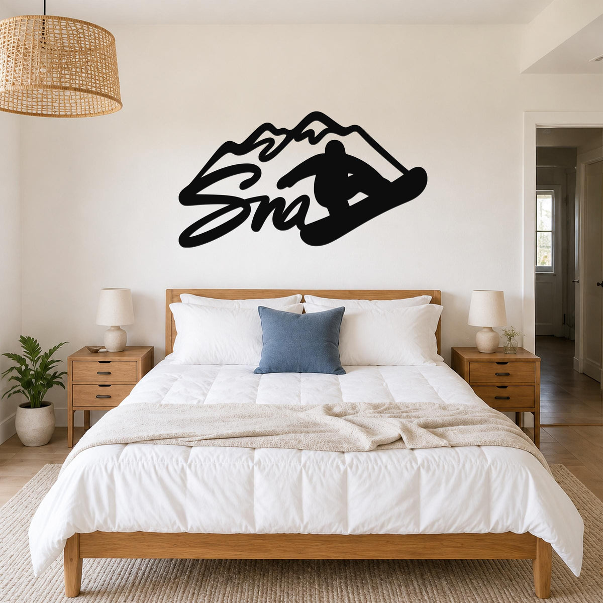 Black metal wall art silhouette of a snowboarder in motion with mountain peaks, mounted above a bed in a bedroom.