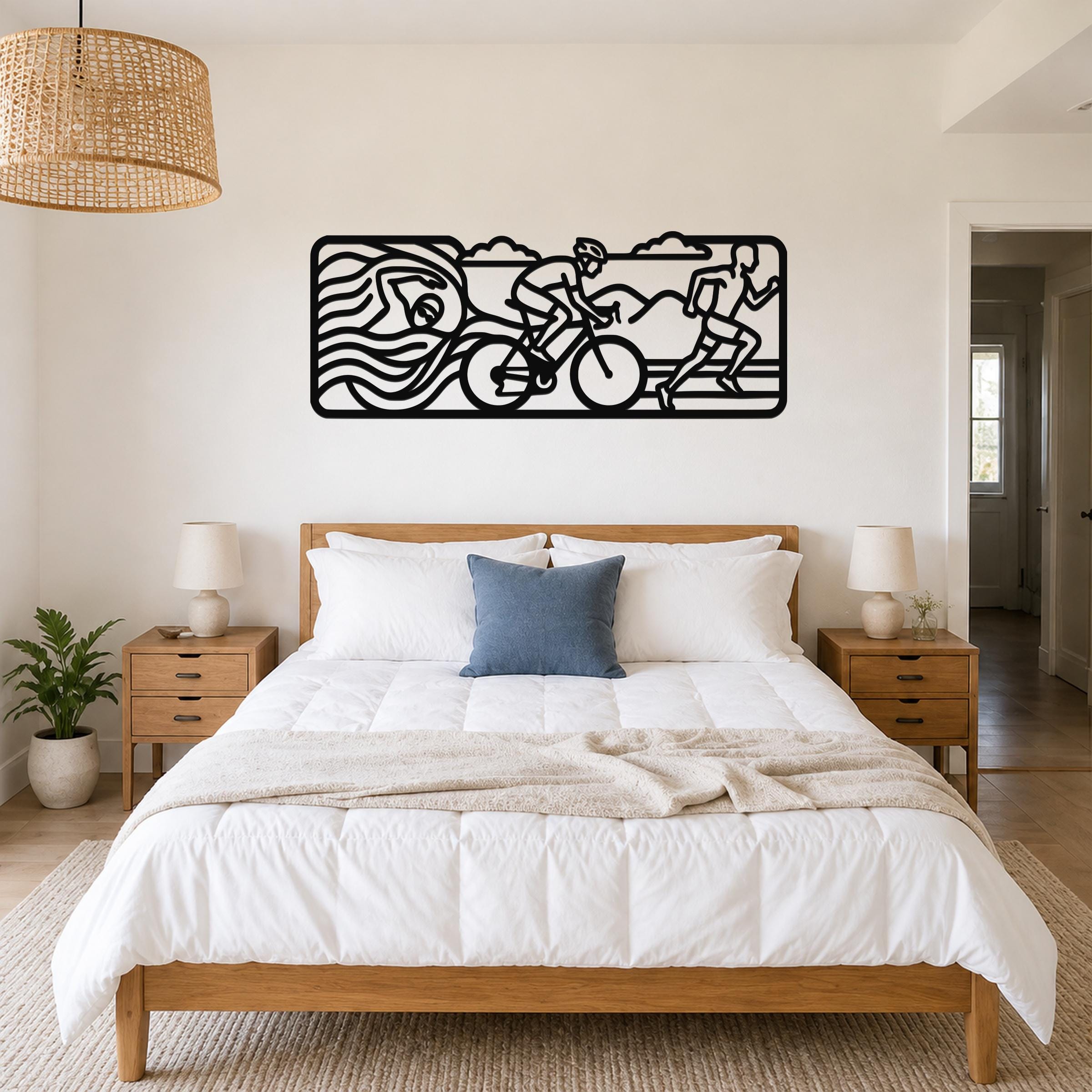 Black metal triathlon wall art with swim, bike, and run silhouettes, mounted above a bed in a bedroom.