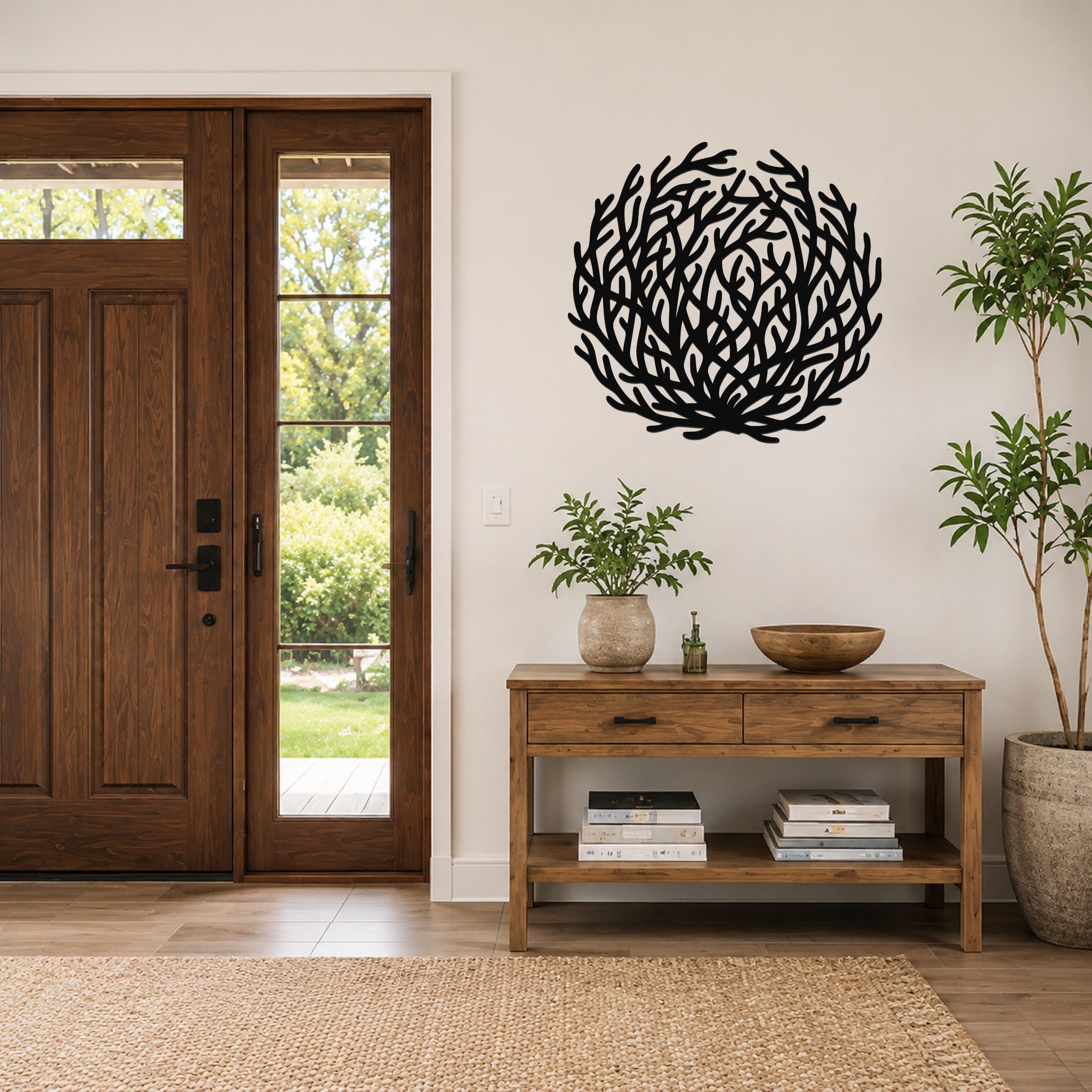Black metal wall art in a circular, branch-like cutout design, mounted on a white wall above a wooden console table in a entryway.