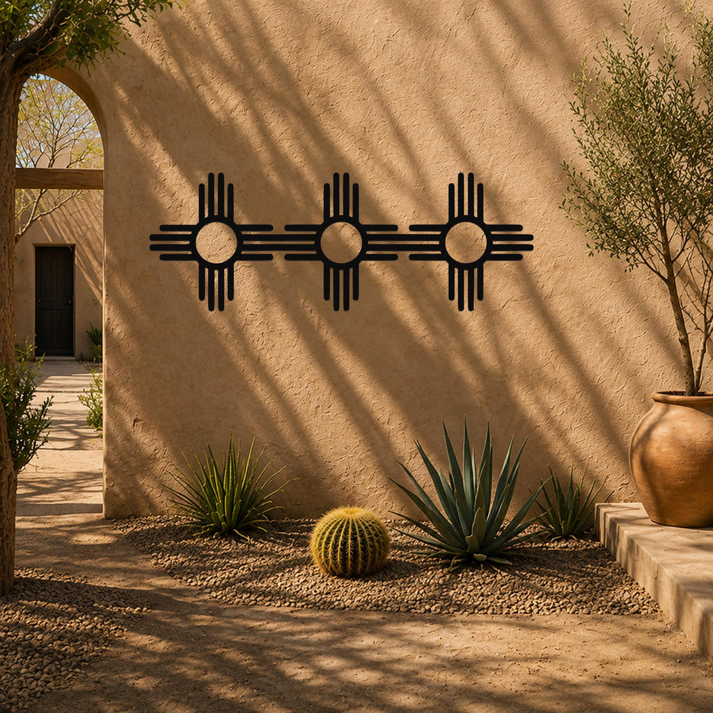 Black metal Zia Sun symbol trio wall art with four rays on each of three connected suns, mounted on a stucco outdoor wall above a desert garden with cacti and gravel.