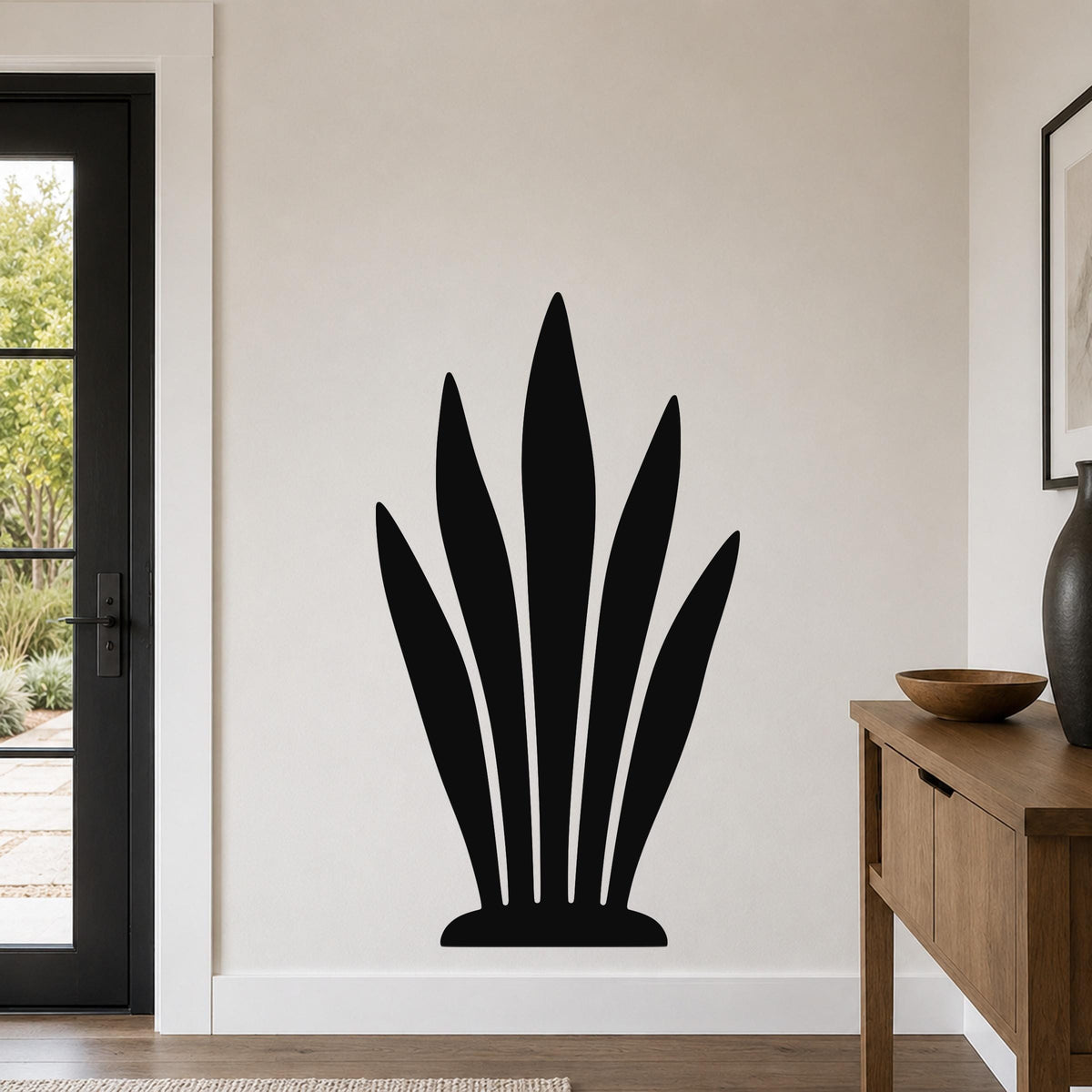 Black metal wall art in a silhouette of a snake plant, mounted on a light-colored wall in a modern entryway.