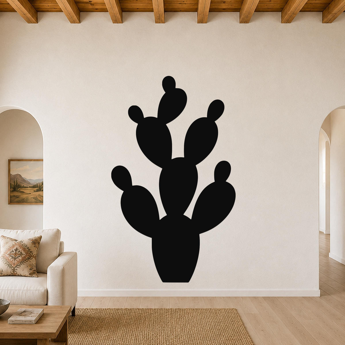 Black metal prickly pear cactus wall art with multiple rounded pads and cutout details, mounted on a living room wall above a sofa.