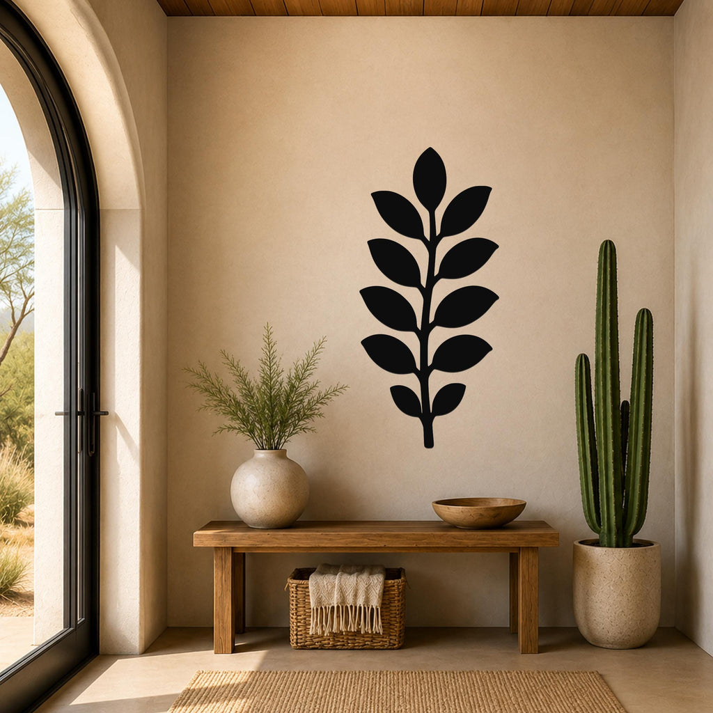Black metal leaf wall art with a vertical branch and multiple leaf cutouts, mounted on a beige wall above a wooden bench in a sunlit entryway.