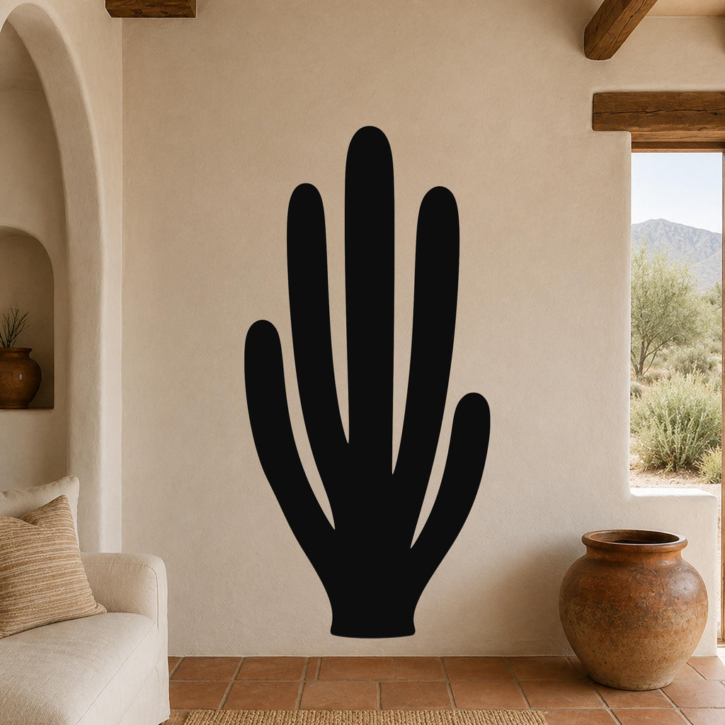 Black metal wall art in the silhouette of an organ pipe cactus, mounted on a beige stucco wall in a living room with terracotta flooring and wooden beams.