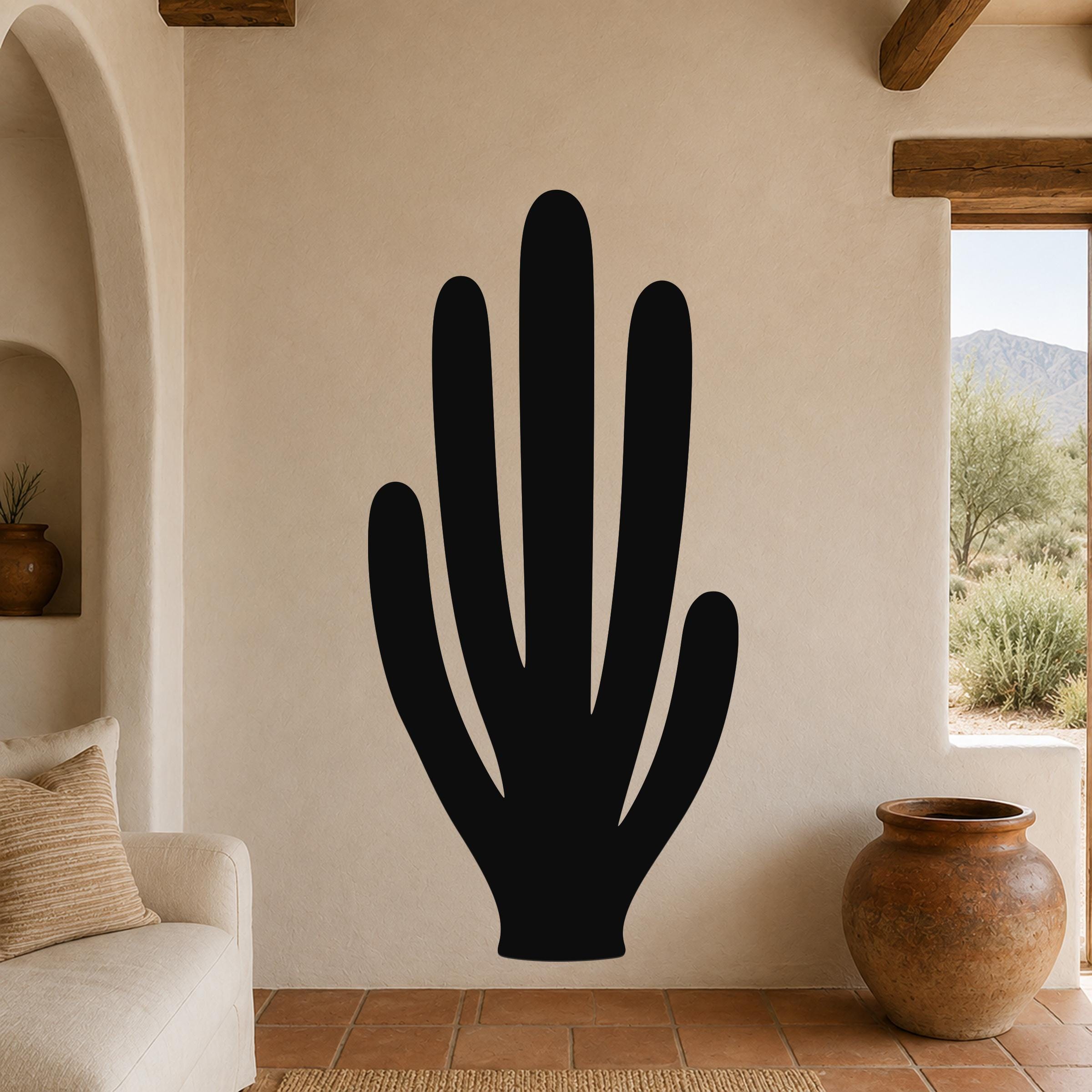 Black metal wall art in the silhouette of an organ pipe cactus, mounted on a beige stucco wall in a living room with terracotta flooring and wooden beams.