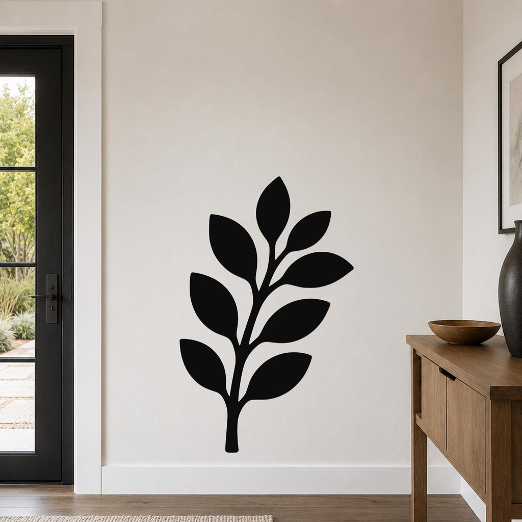 Black metal wall art in a leafy branch silhouette, mounted on a light-colored wall above a wooden console table in a modern entryway.