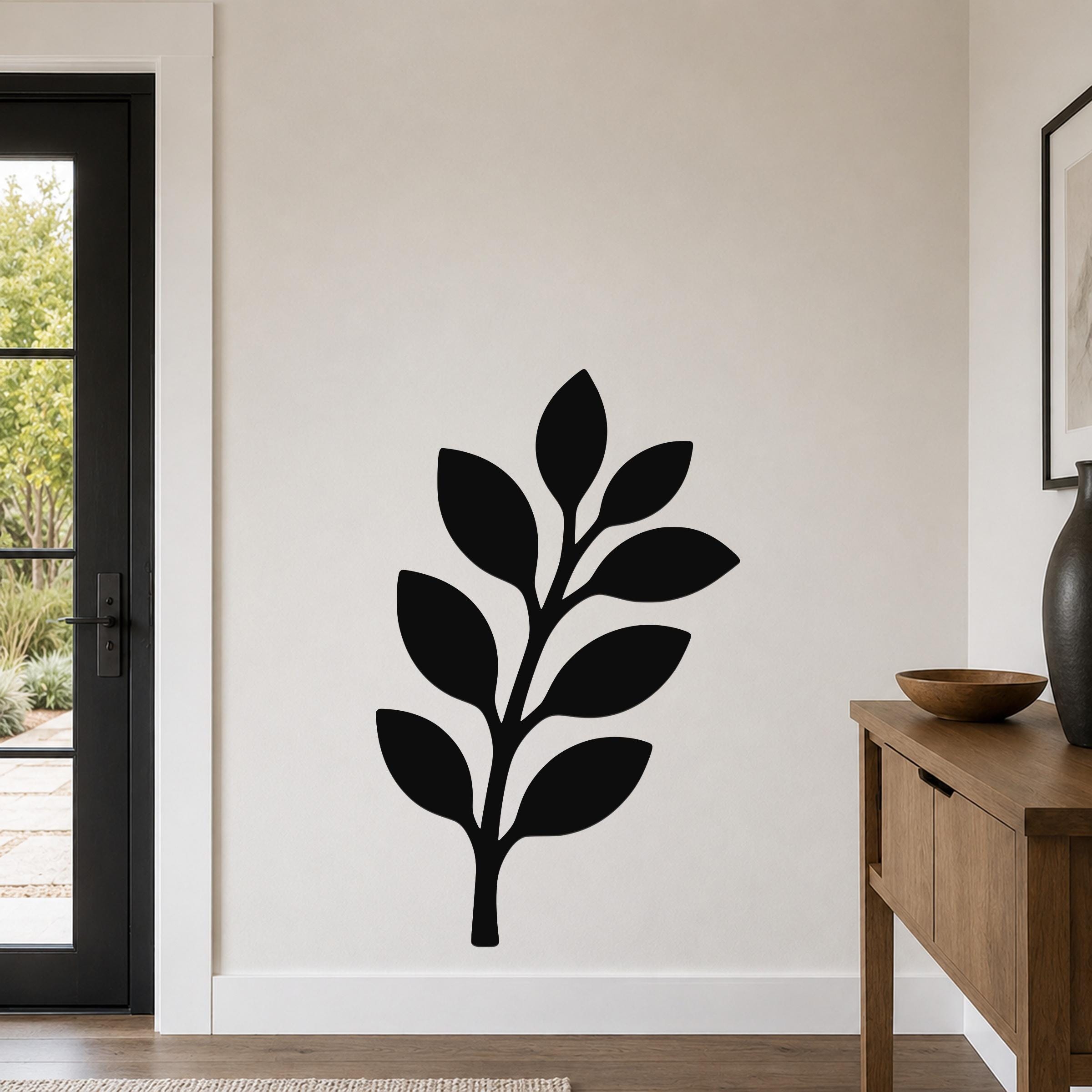 Black metal wall art in a leafy branch silhouette, mounted on a light-colored wall above a wooden console table in a modern entryway.
