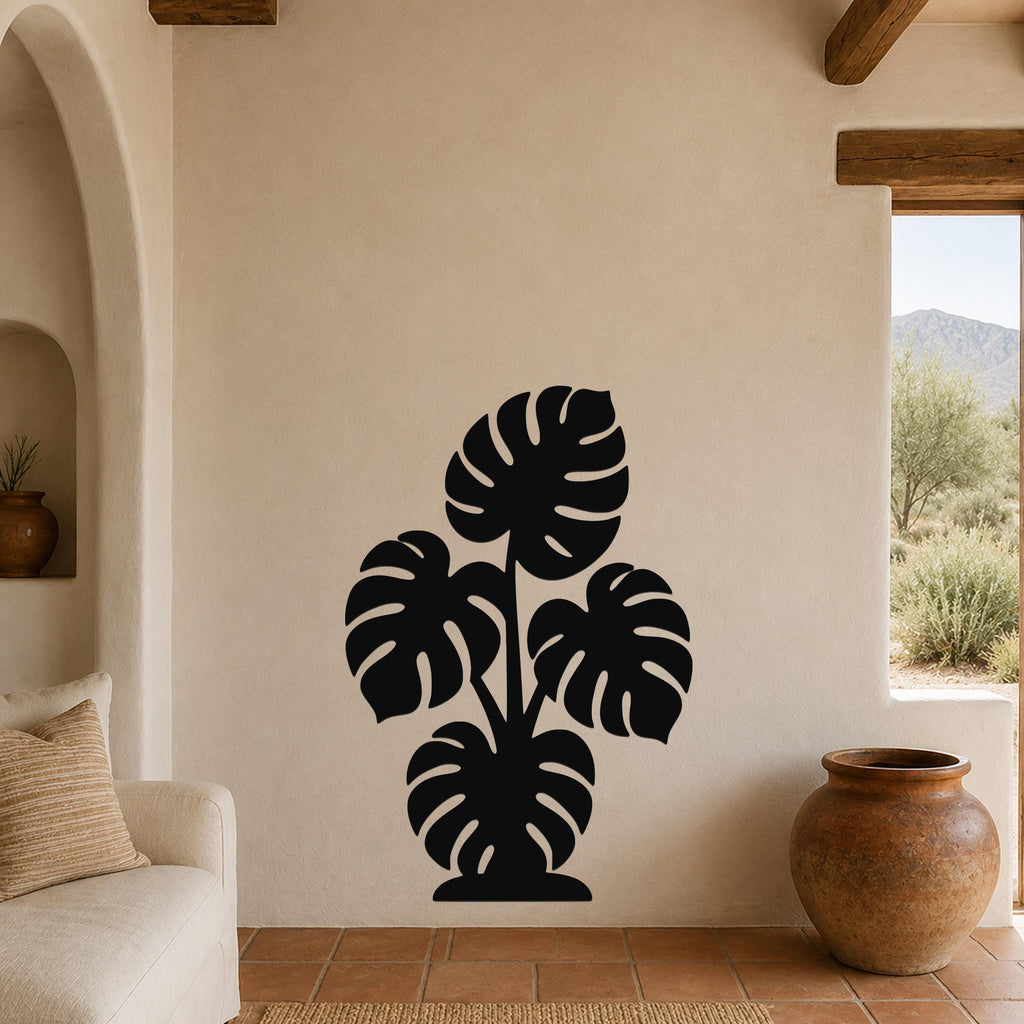Black metal wall art silhouette of a monstera plant with multiple leaf cutouts, mounted on a beige living room wall above a tiled floor.