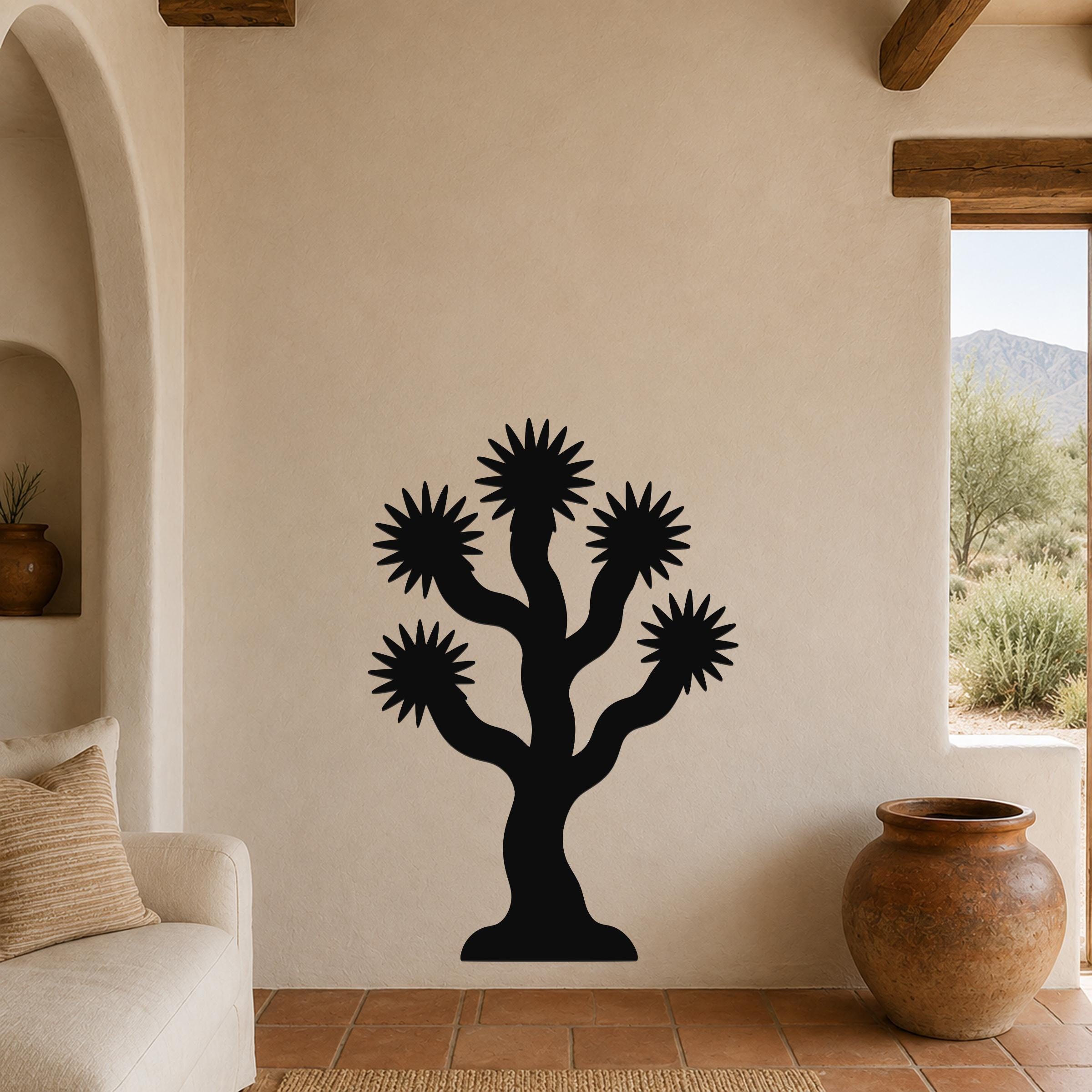 Black metal Joshua tree wall art with starburst-shaped branches, mounted on a beige stucco wall in a living room with terracotta flooring and wooden beams.