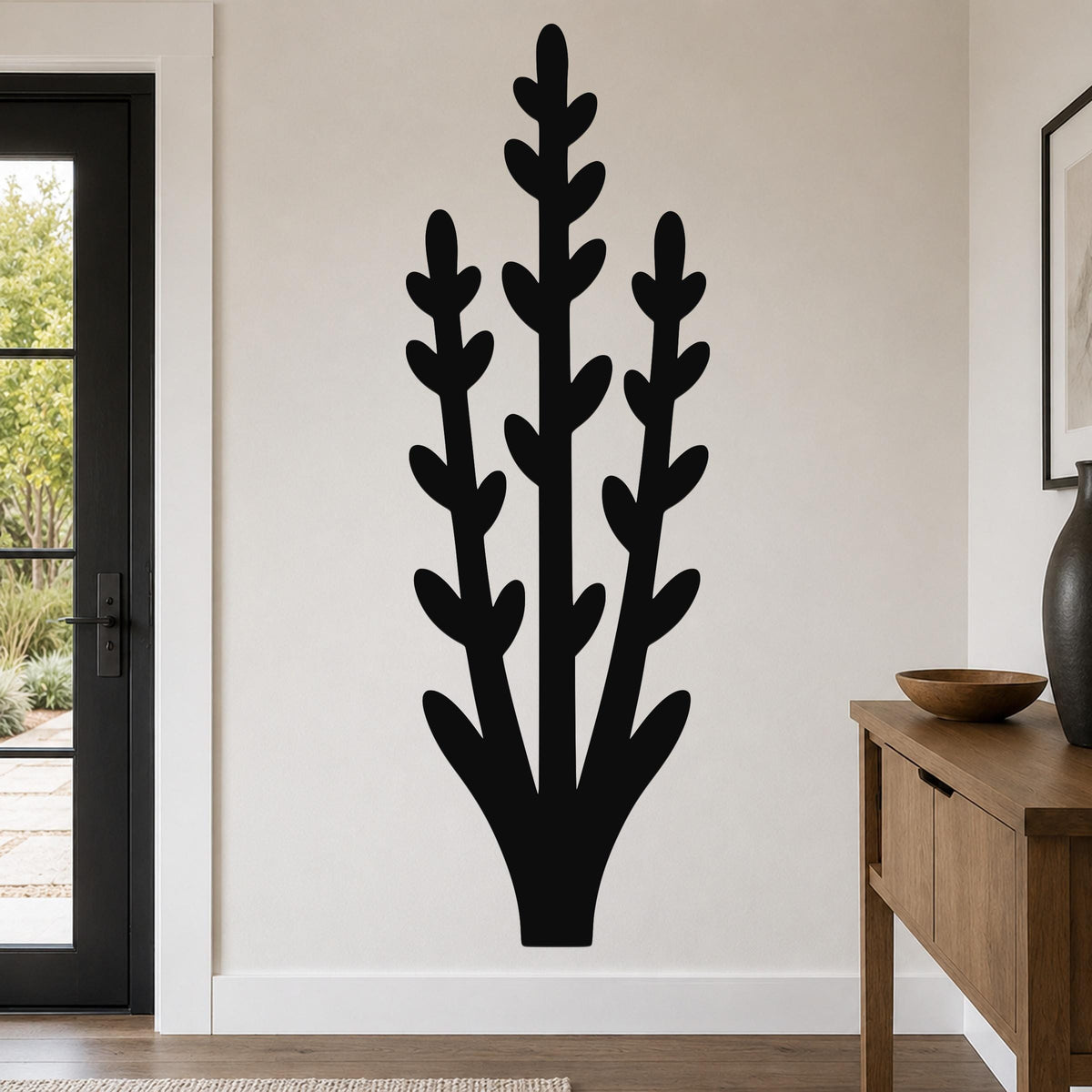 Black metal wall art in a silhouette of an abstract desert plant with layered leafy stems, mounted on a living room wall above a wooden console table.
