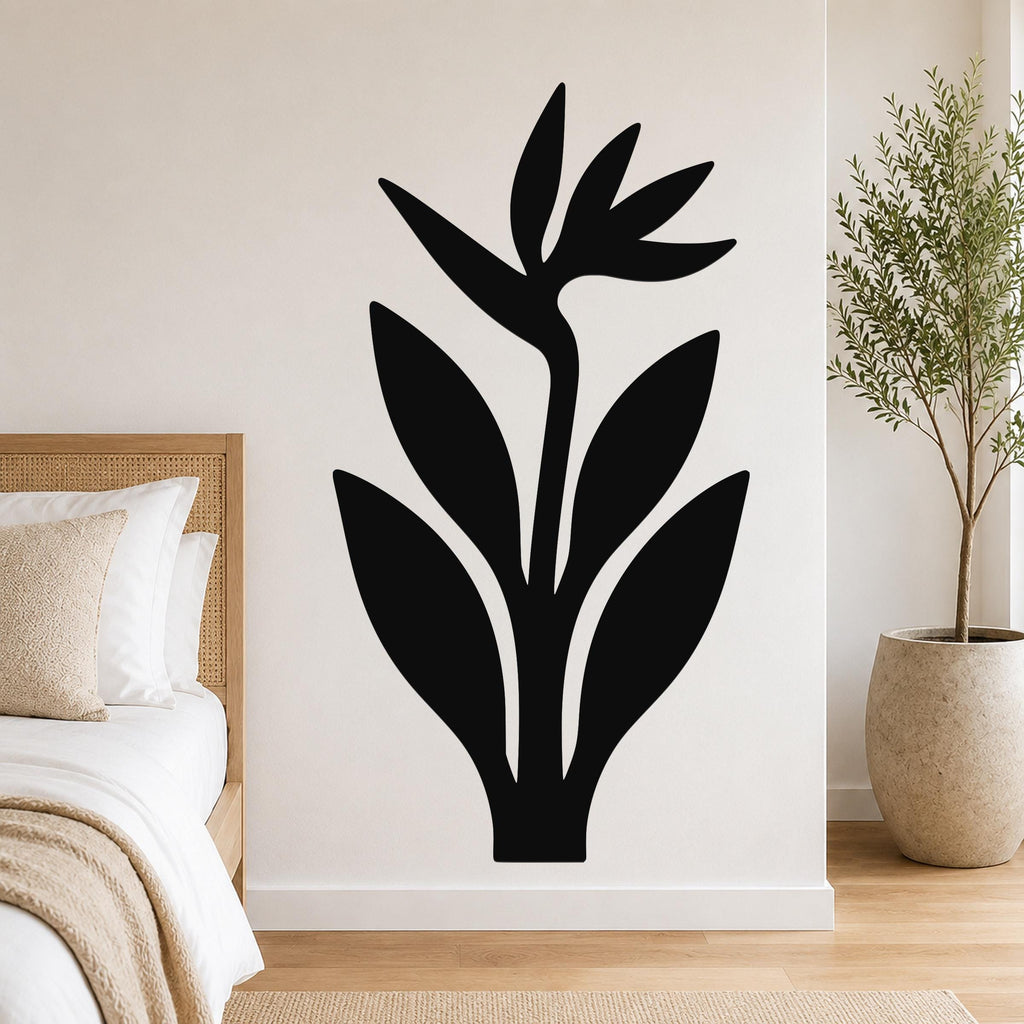 Black metal Bird of Paradise wall art with leaf and flower cutouts, mounted on a bedroom wall above a bed.