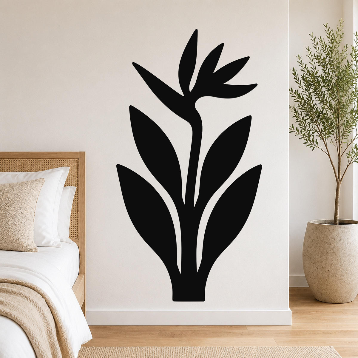 Black metal Bird of Paradise wall art with leaf and flower cutouts, mounted on a bedroom wall above a bed.