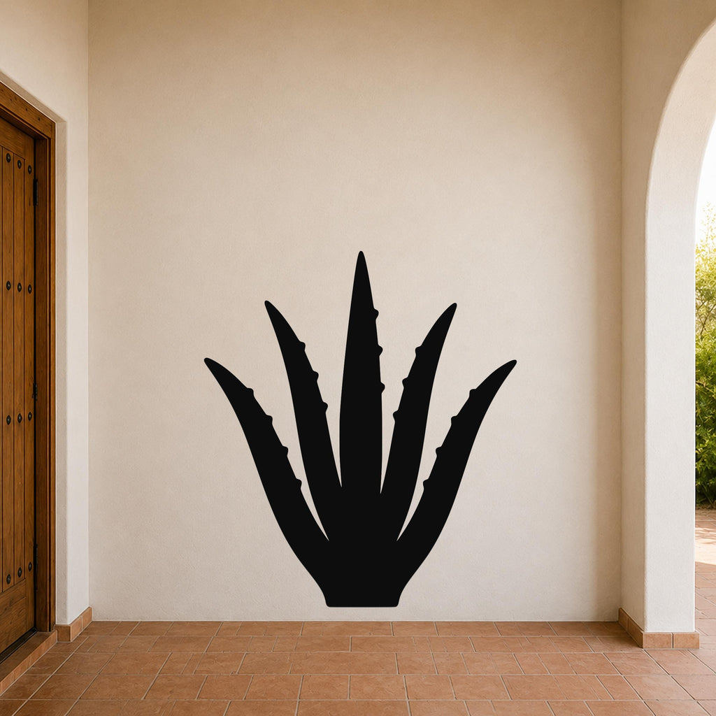 Black metal agave wall art with spiky leaf cutouts, mounted on a beige stucco wall in a covered entryway with terracotta flooring.