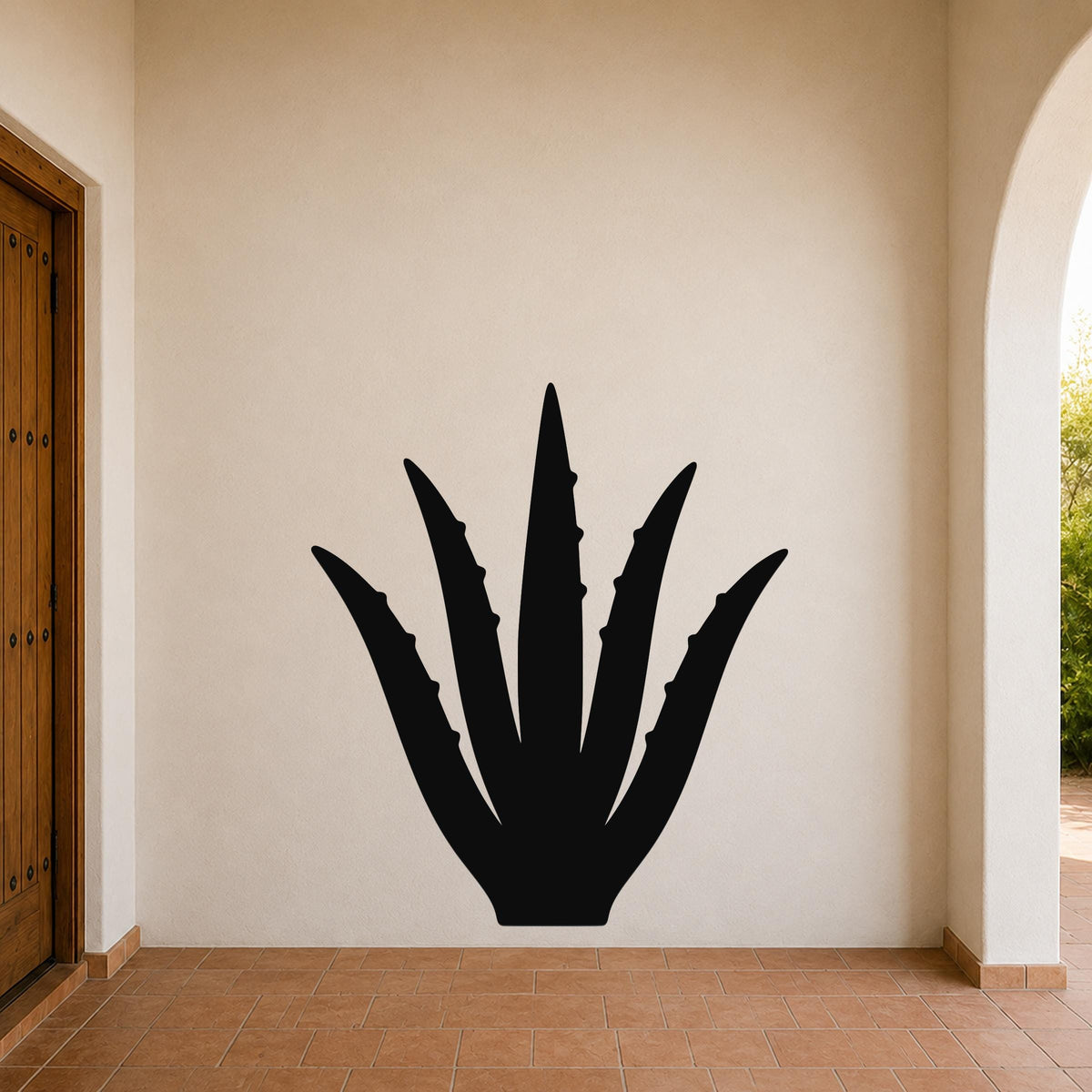 Black metal agave wall art with spiky leaf cutouts, mounted on a beige stucco wall in a covered entryway with terracotta flooring.