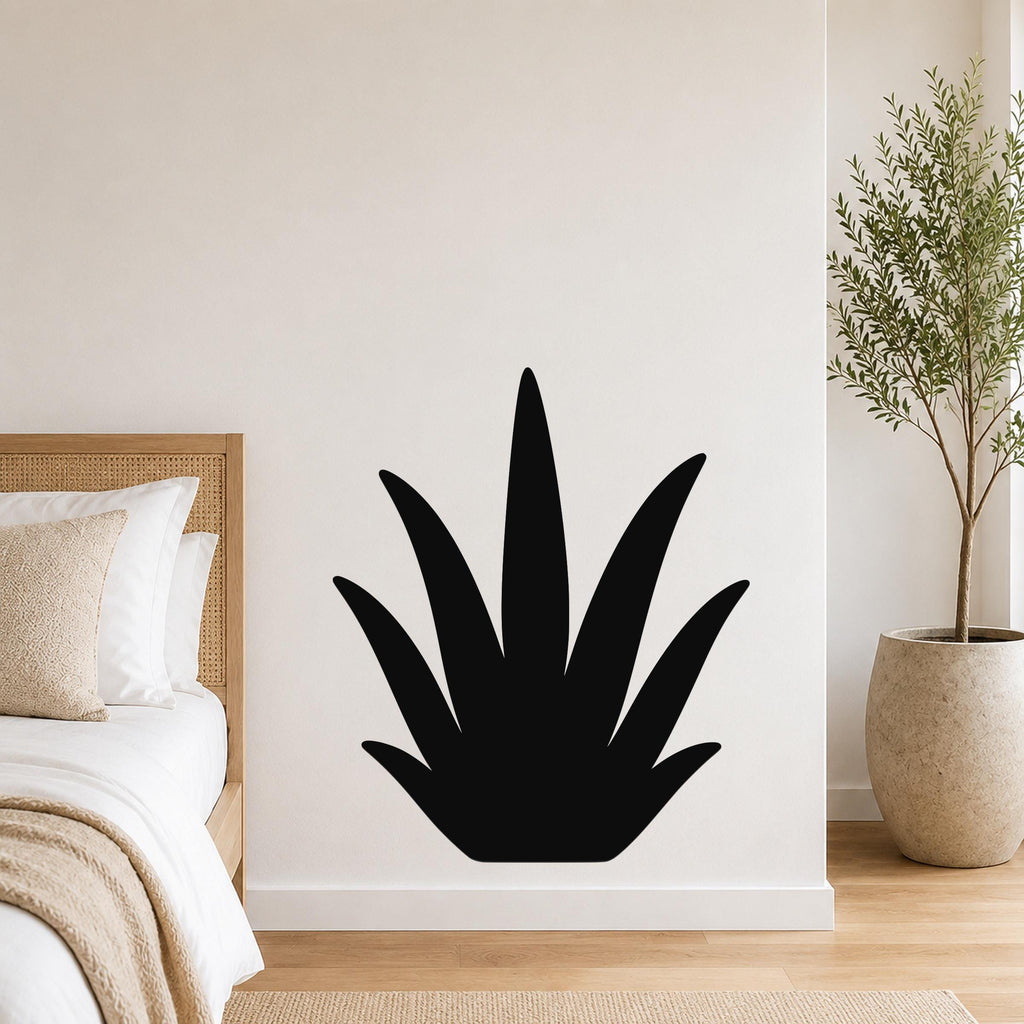 Black metal agave wall art silhouette mounted on a white bedroom wall above a bed with a woven headboard.