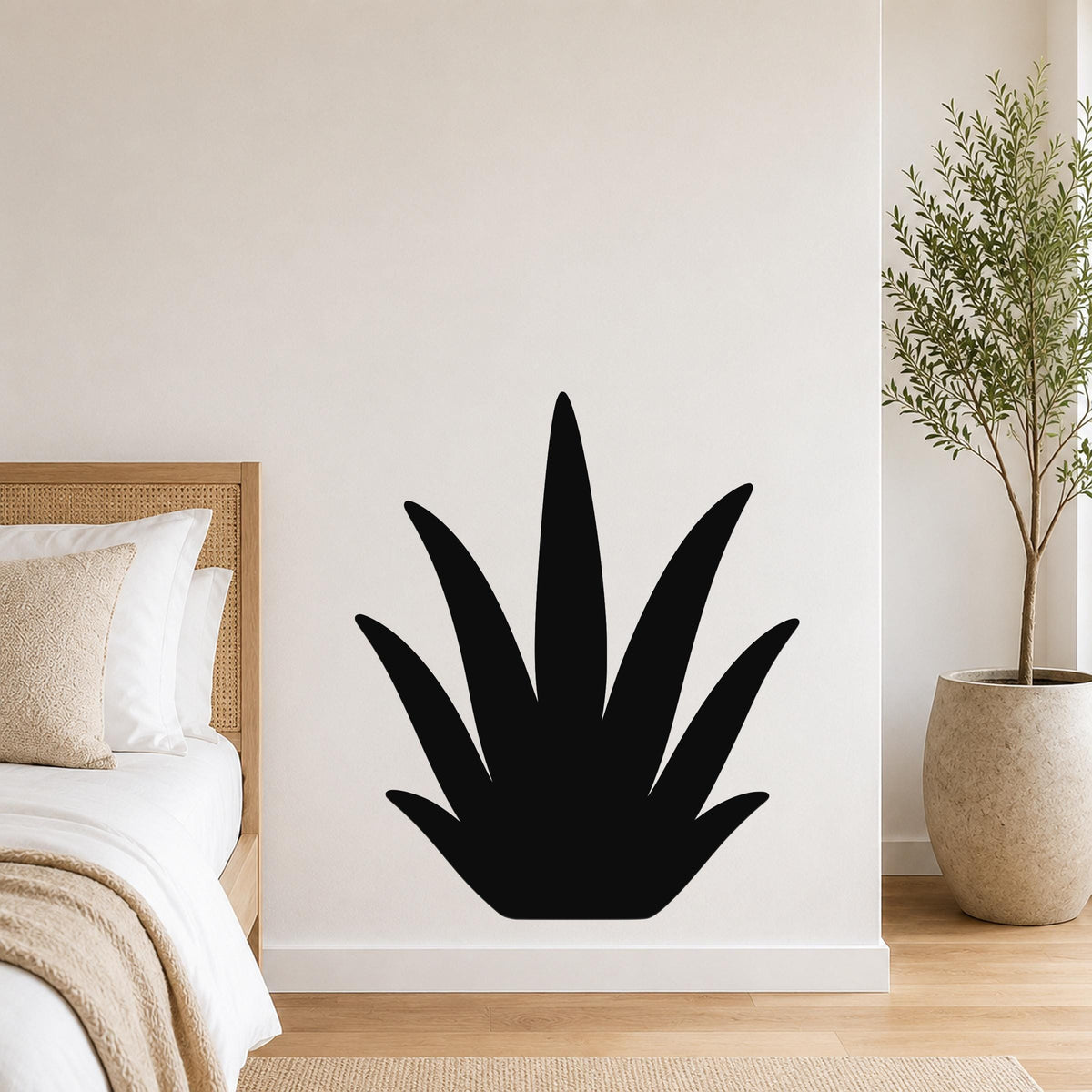 Black metal agave wall art silhouette mounted on a white bedroom wall above a bed with a woven headboard.