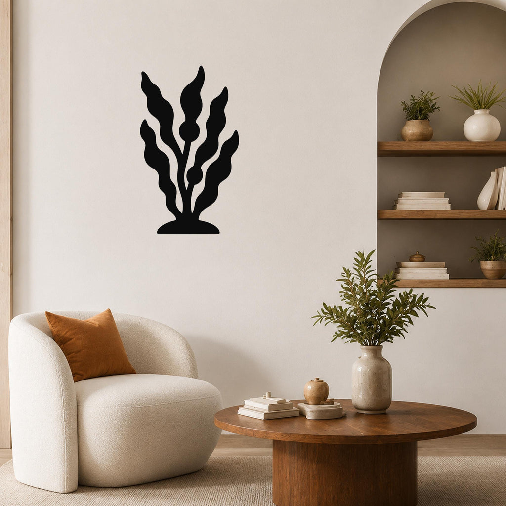 Black metal kelp wall art with wavy leaf cutouts, mounted on a living room wall above a white armchair.