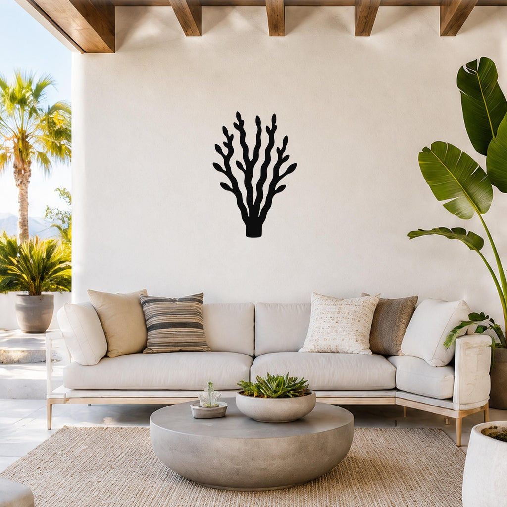 Black metal kelp wall art with branching cutouts, mounted on a white wall above a light-colored sofa in a coastal living room.
