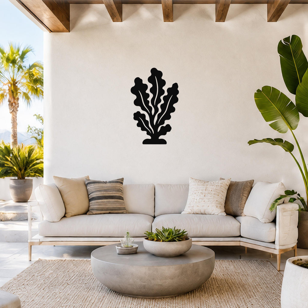 Black metal kelp wall art with leafy cutout design, mounted on a white wall above a light-colored sofa in a bright living room.