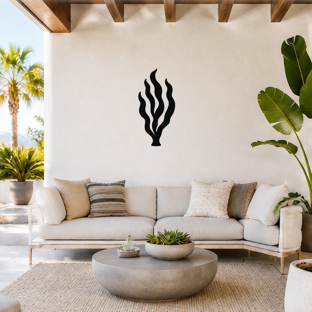 Black metal kelp seaweed wall art with flowing frond cutouts, mounted on a white wall above a light-colored sofa in a bright living room.