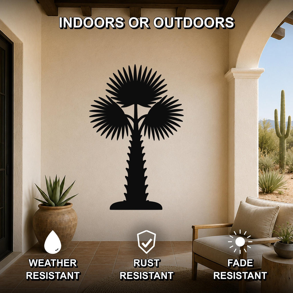 Black metal palm tree wall art with fan-shaped fronds and a textured trunk, mounted on a beige wall in a covered patio with outdoor furniture and desert plants.