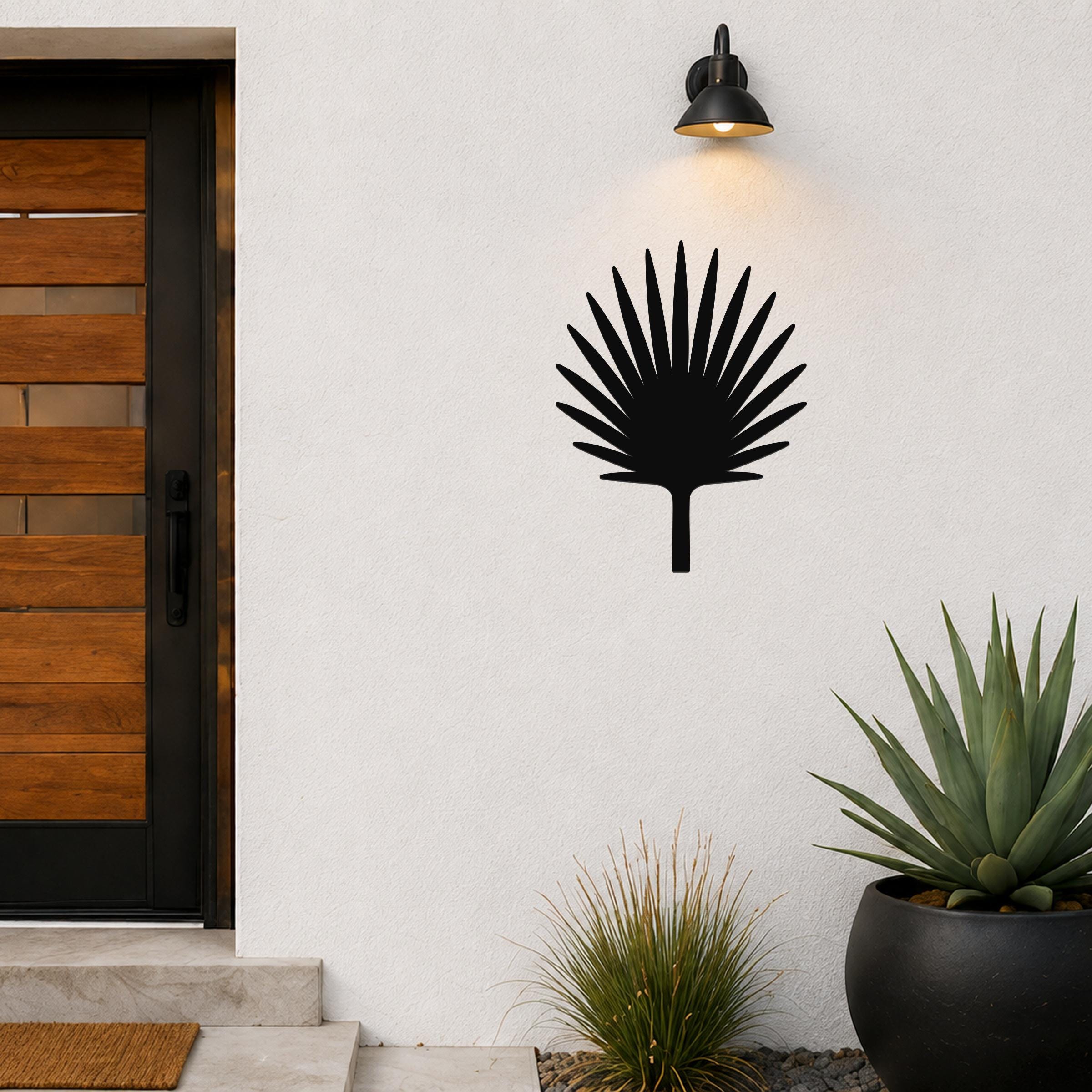 Black metal fan palm tree wall art with radiating leaf cutouts, mounted on an outdoor wall beside a door and potted plants.