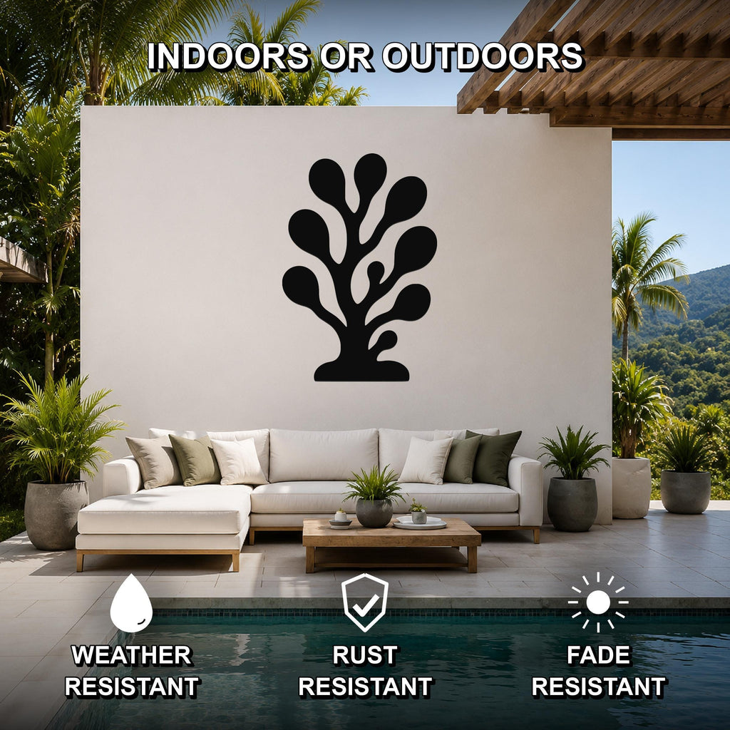 Black metal coral wall art with organic cutout design, mounted on a white outdoor wall above a sofa in a patio living area.