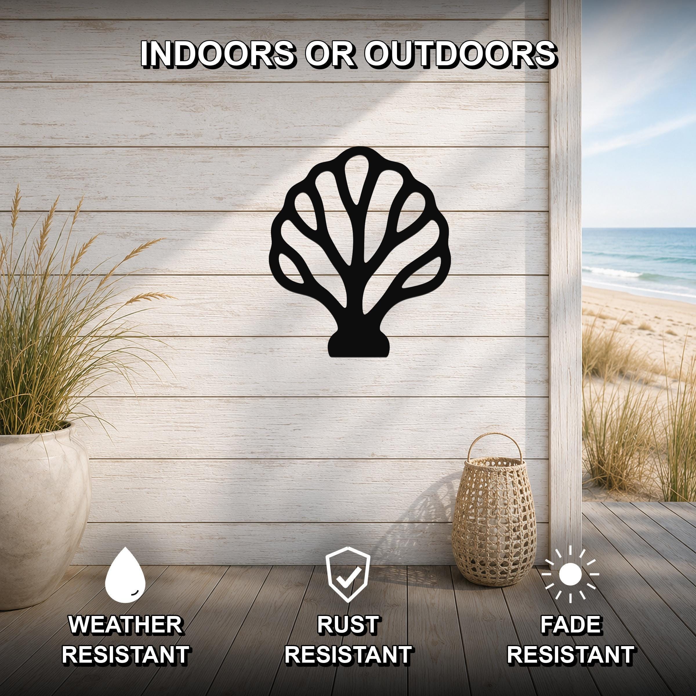 Black metal fan coral wall art with intricate cutout details, mounted on a light wood wall in an outdoor patio setting with a beach view.