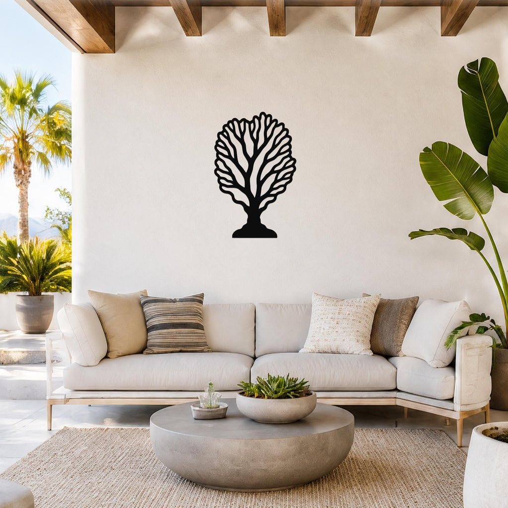 Black metal fan coral wall art with intricate branch cutouts, mounted on a white wall above a light-colored sofa in a bright living room.
