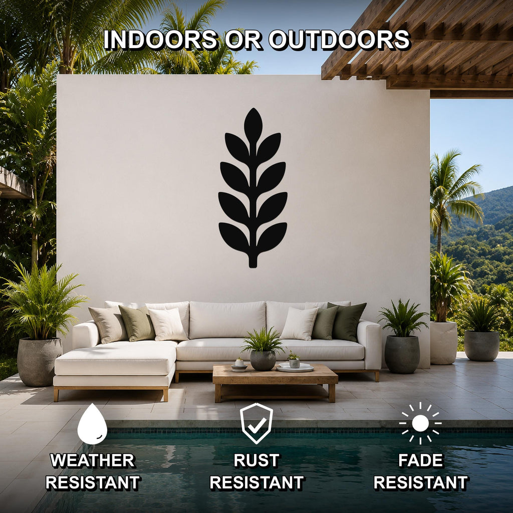 Black metal botanical sprig wall art with leaf cutouts, mounted on a white outdoor wall above a sofa in a patio living area.