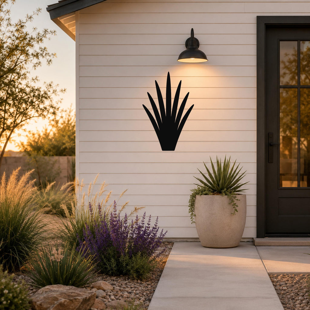 Black metal yucca wall art silhouette mounted on a white siding wall above a patio, illuminated by a wall sconce.