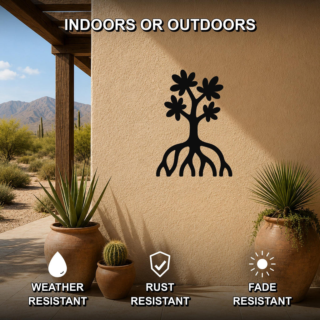 Black metal wall art featuring a tree silhouette with blossoms and visible roots, mounted on an outdoor stucco wall in a desert patio setting with potted plants.