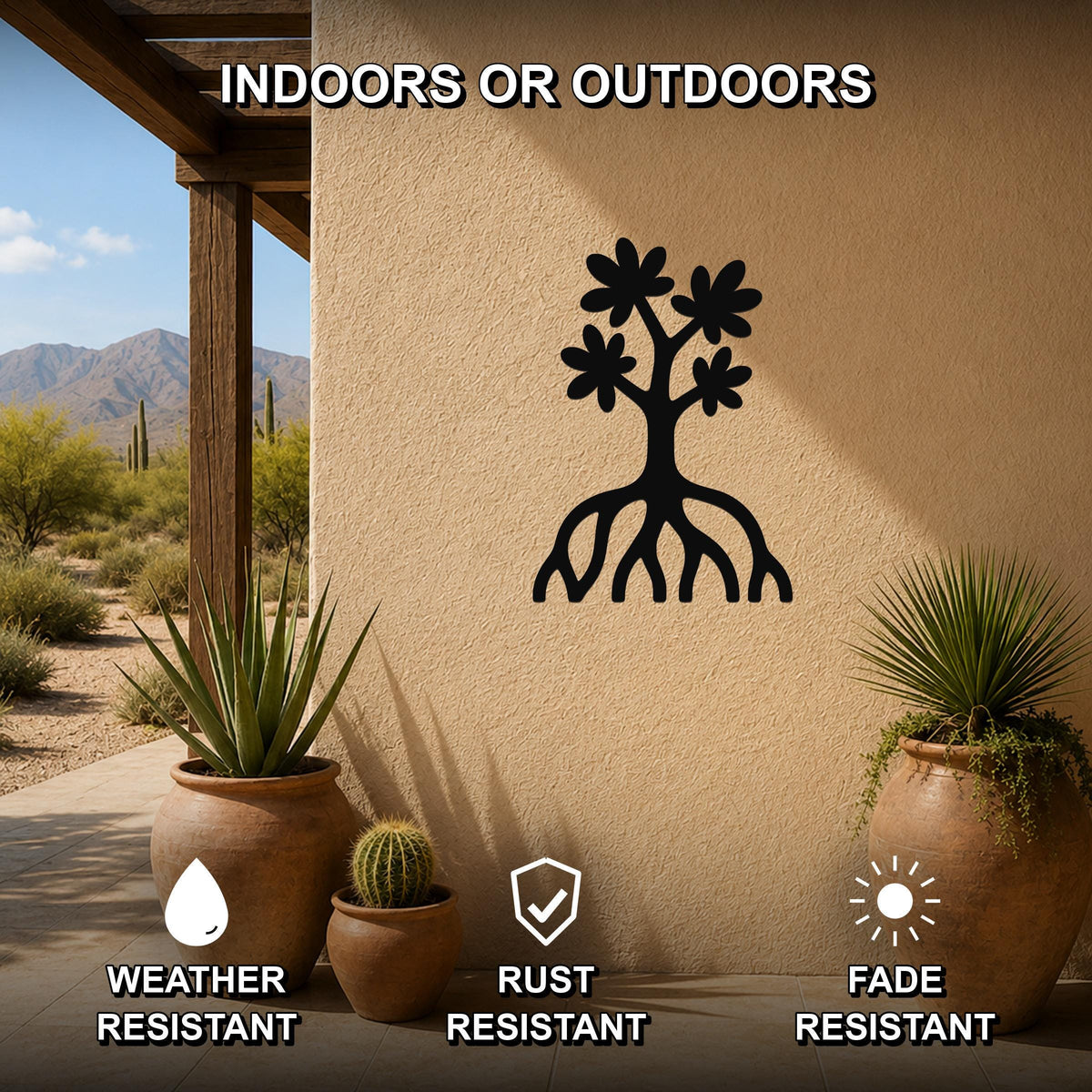 Black metal wall art featuring a tree silhouette with blossoms and visible roots, mounted on an outdoor stucco wall in a desert patio setting with potted plants.