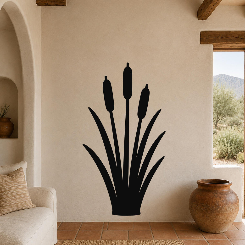 Black metal cattail wall art silhouette with three seed heads and long leaves, mounted on a beige living room wall above a sofa.