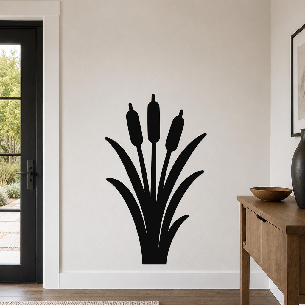 Black metal cattail wall art silhouette with three seed heads and long leaves, mounted on a white wall in a living room near a door and console table.