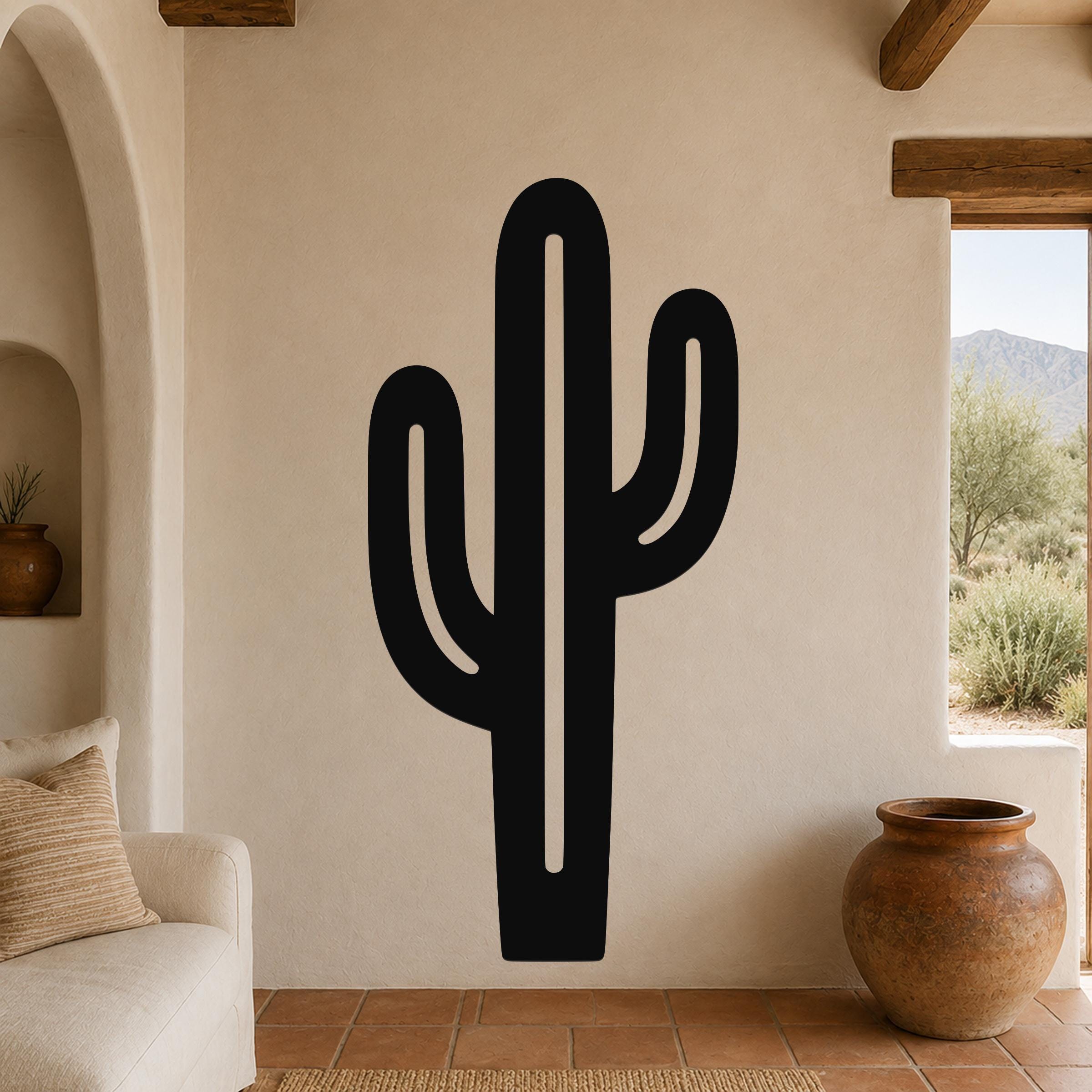 Black metal saguaro cactus wall art with cutout arms, mounted on a beige living room wall above a sofa.