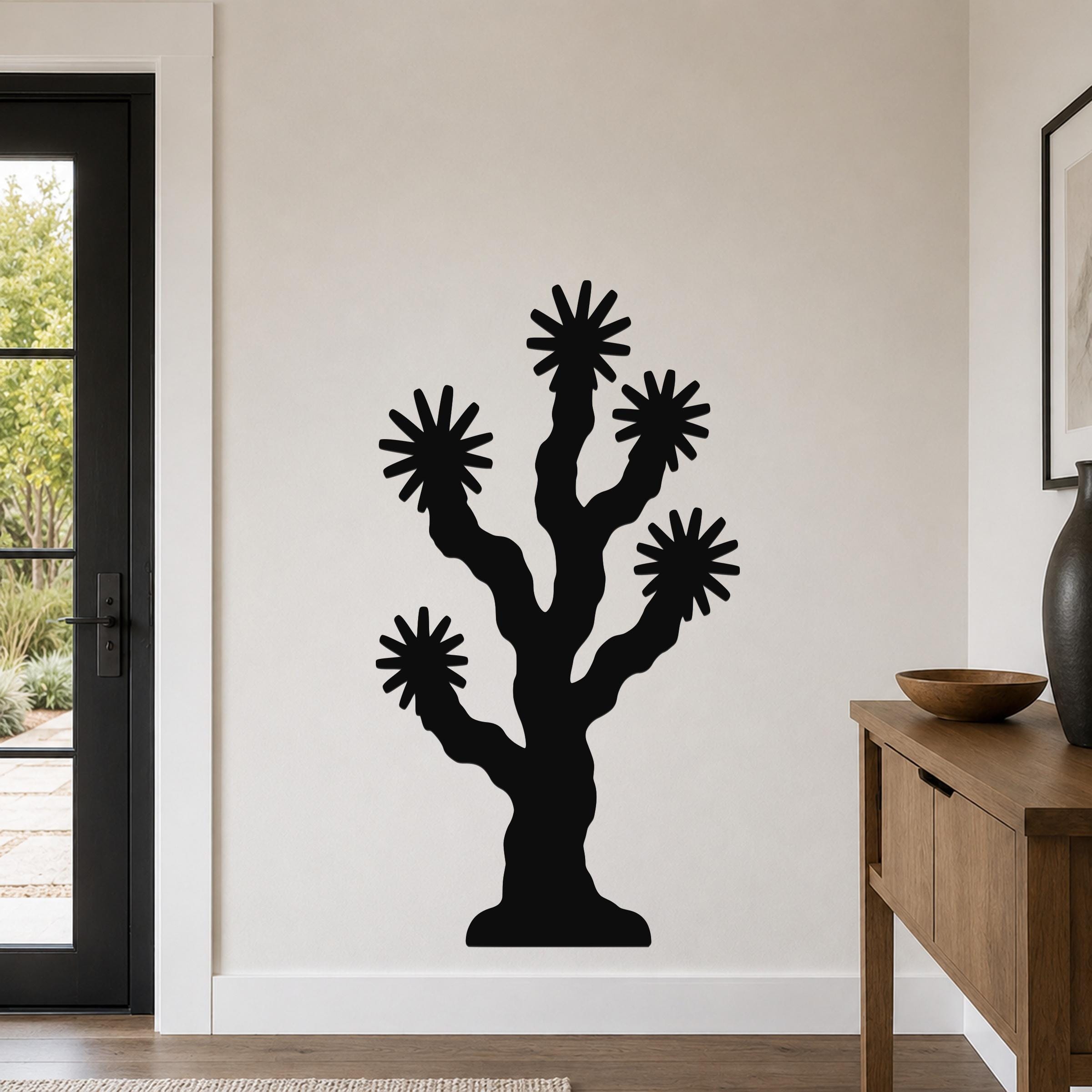 Black metal Joshua tree wall art with starburst cutouts, mounted on a light-colored wall in a modern entryway.