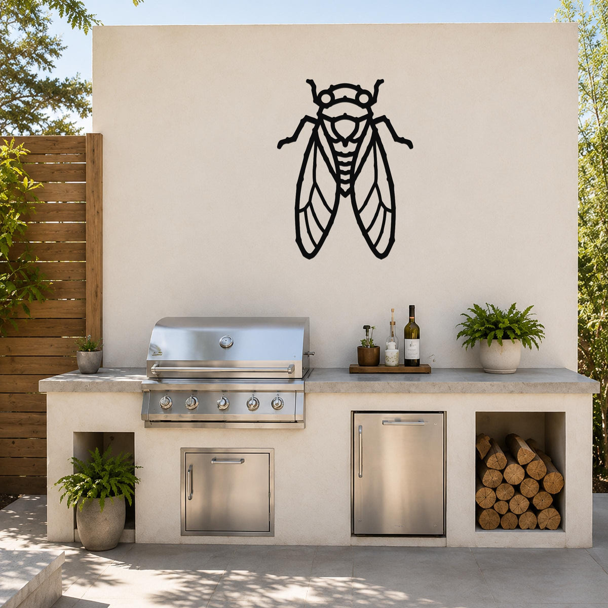 Black metal cicada wall art with detailed wing cutouts, mounted on an outdoor kitchen wall above a stainless steel grill.