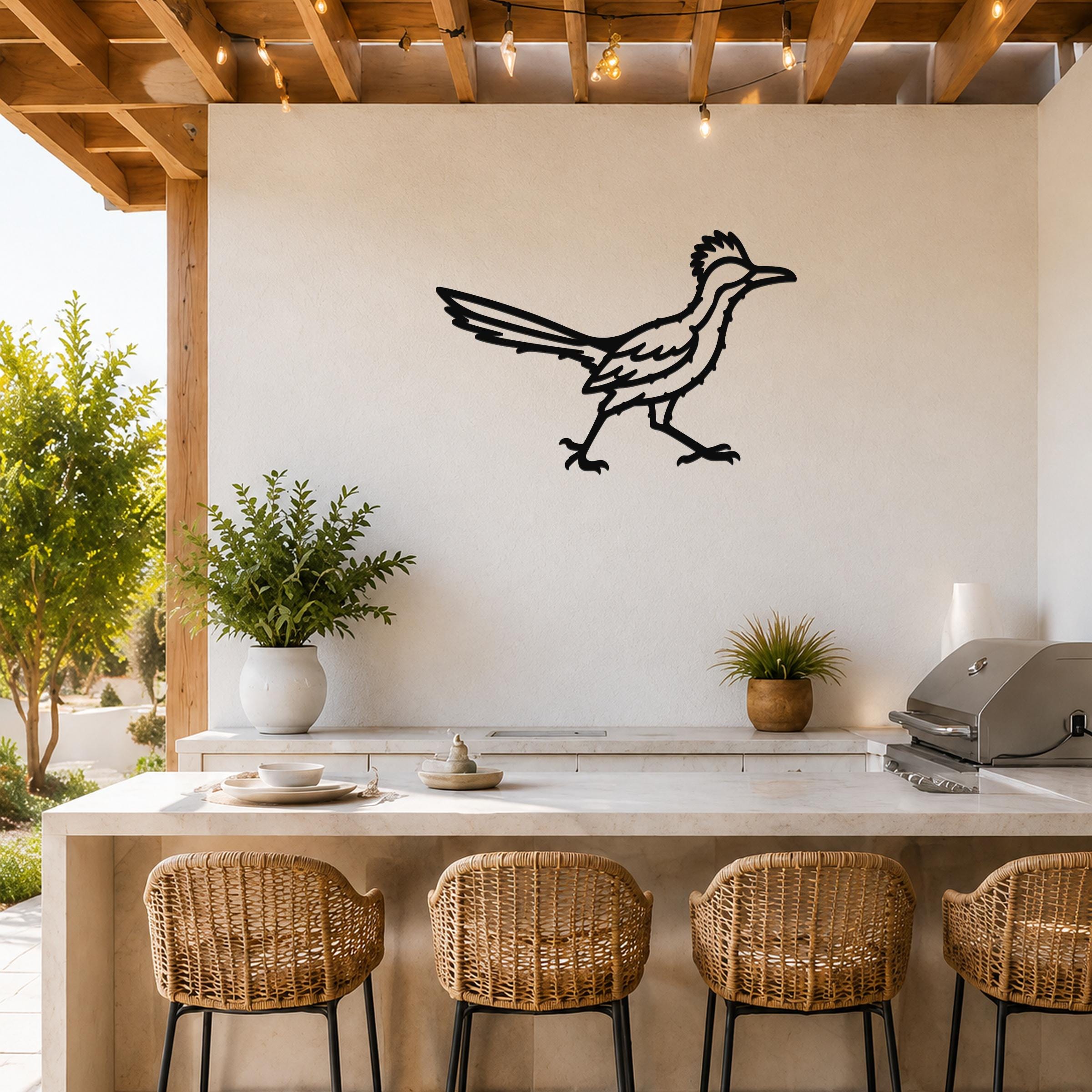 Black metal roadrunner wall art with detailed feather and motion-line cutouts, mounted on a white outdoor wall above a kitchen counter.