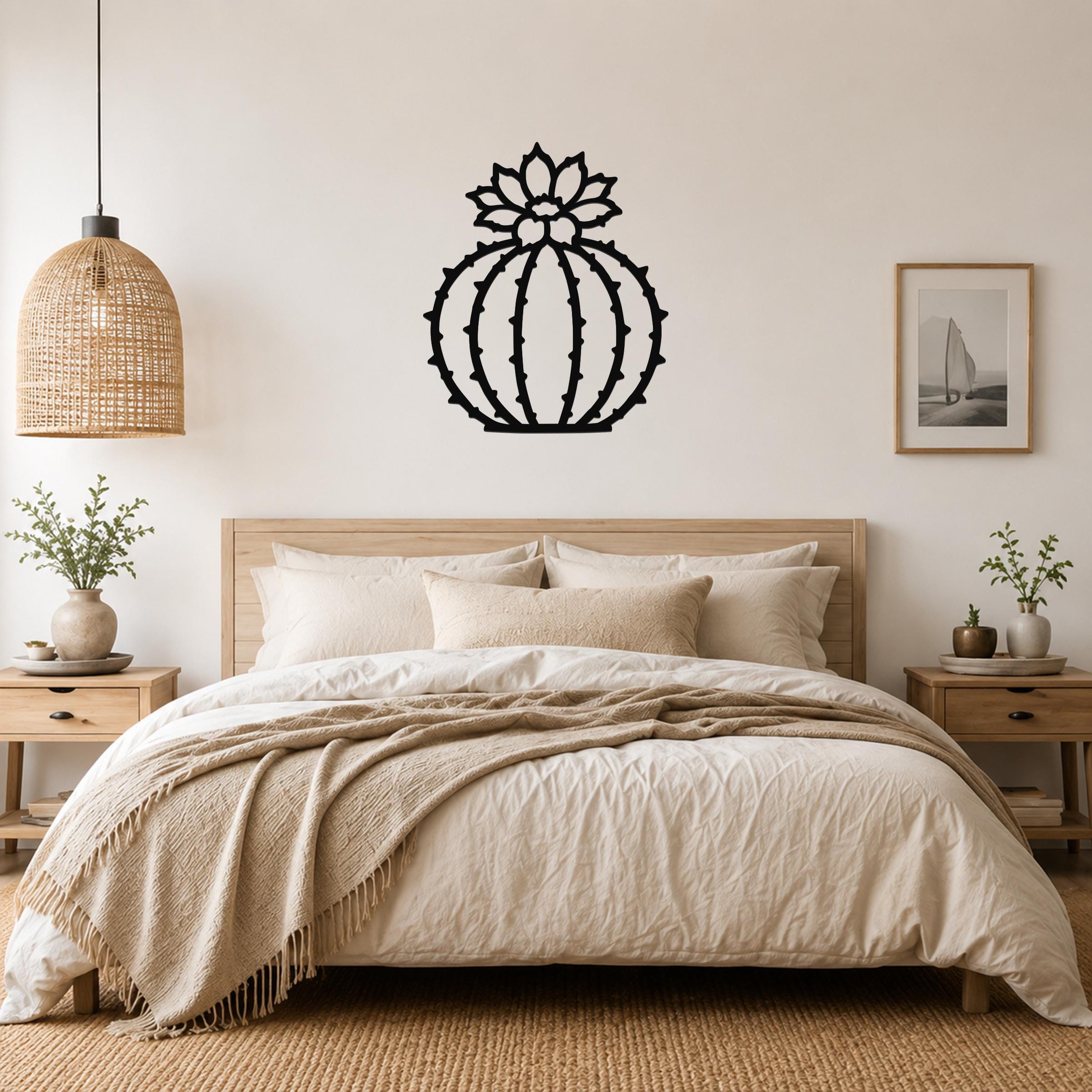 Black metal barrel cactus wall art with flower and spine cutouts, mounted above a bed in a neutral bedroom.