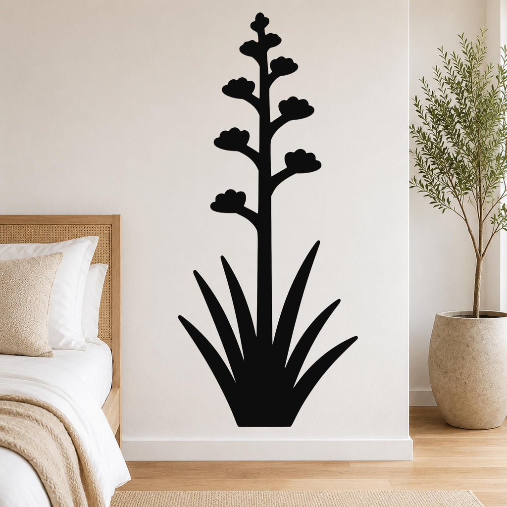 Black metal agave wall art with a tall flowering stalk and spiky leaves, mounted on a white bedroom wall above a bed.
