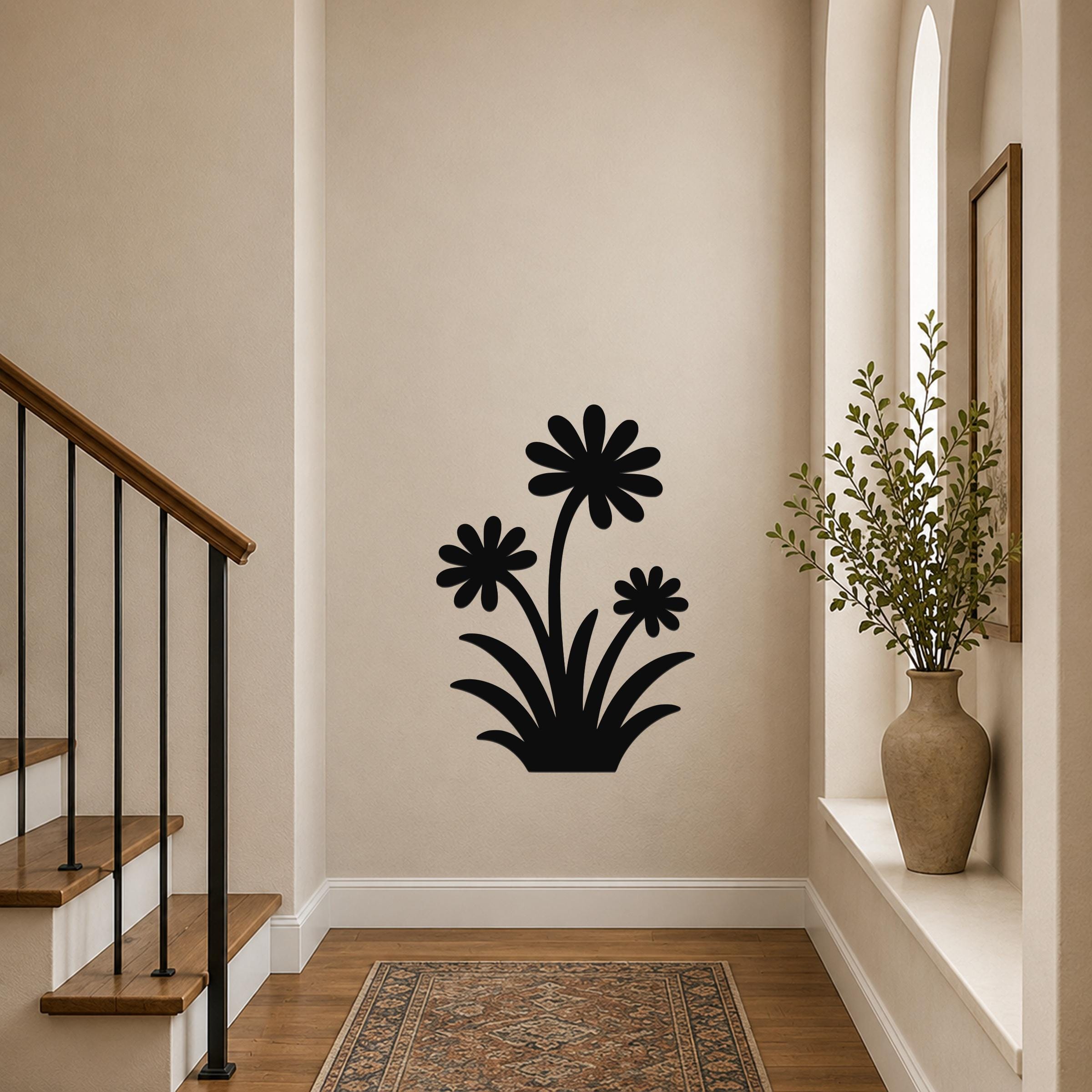 Black metal wall art with a wildflower silhouette of three daisies and leaves, mounted on a hallway wall near a staircase and a window with a potted plant.