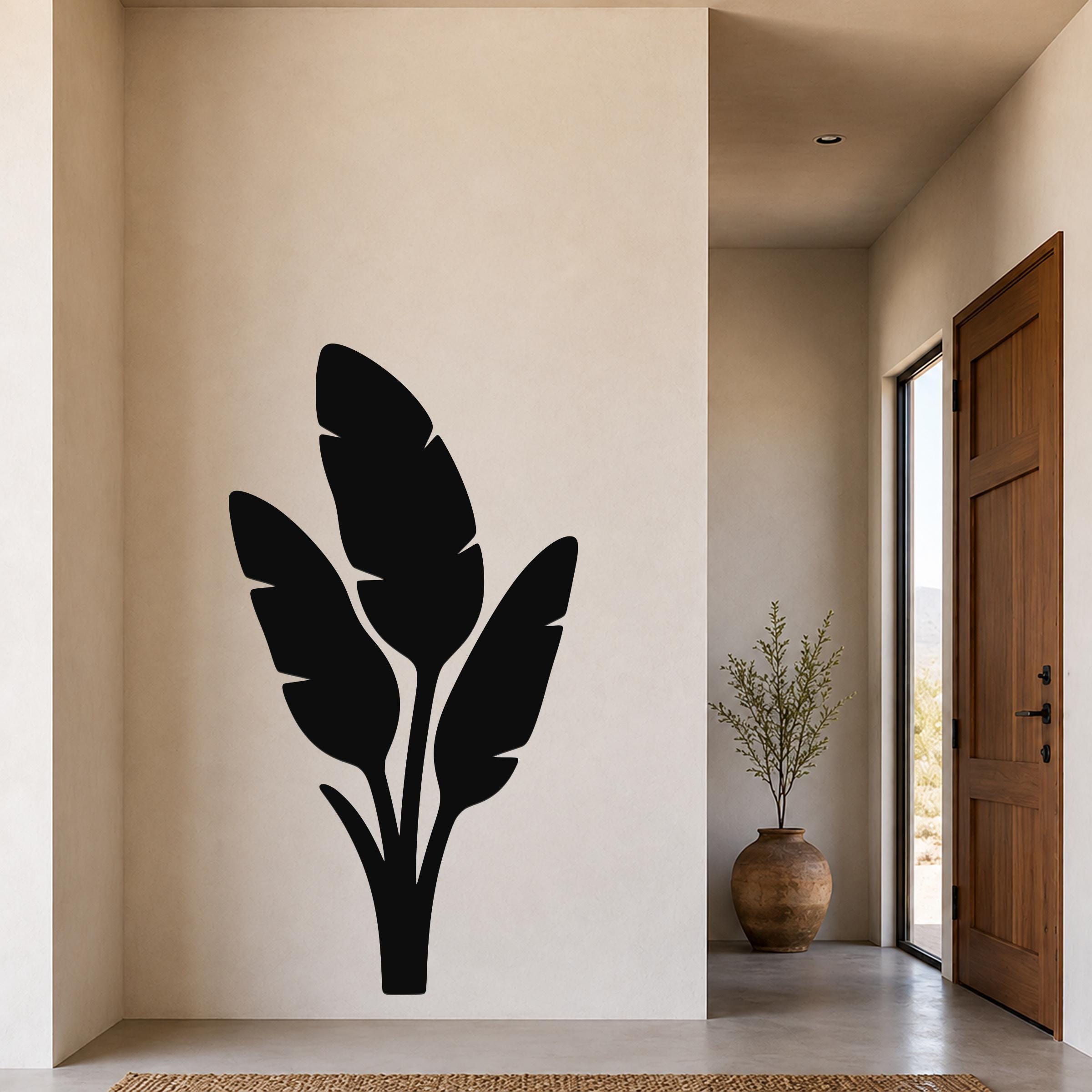 Black metal wall art featuring a tropical leaf silhouette, mounted on a beige wall in a modern entryway.