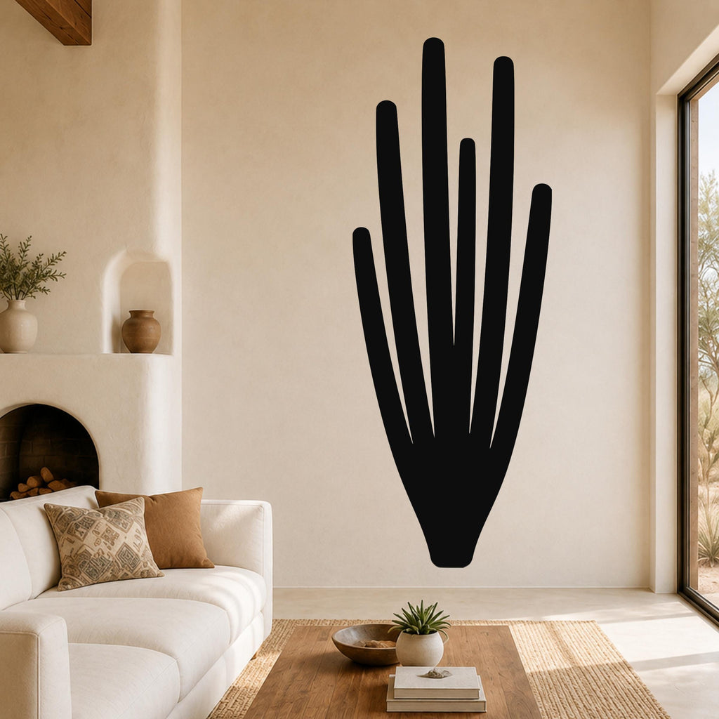Black metal wall art in the shape of an organ pipe cactus with vertical spines, mounted on a living room wall above a white sofa.