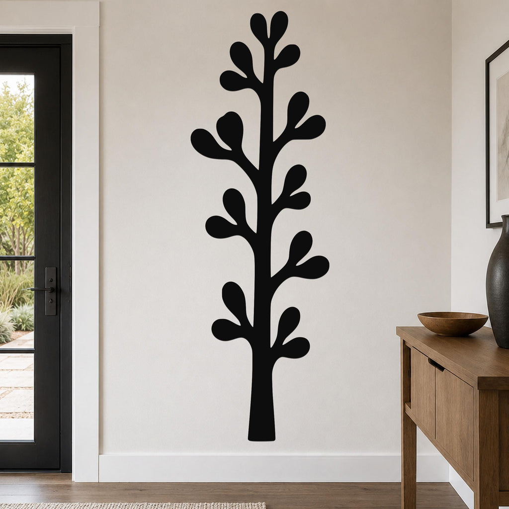 Black metal wall art in a tall, stylized olive branch silhouette with leaf cutouts, mounted on a living room wall above a wooden console table.