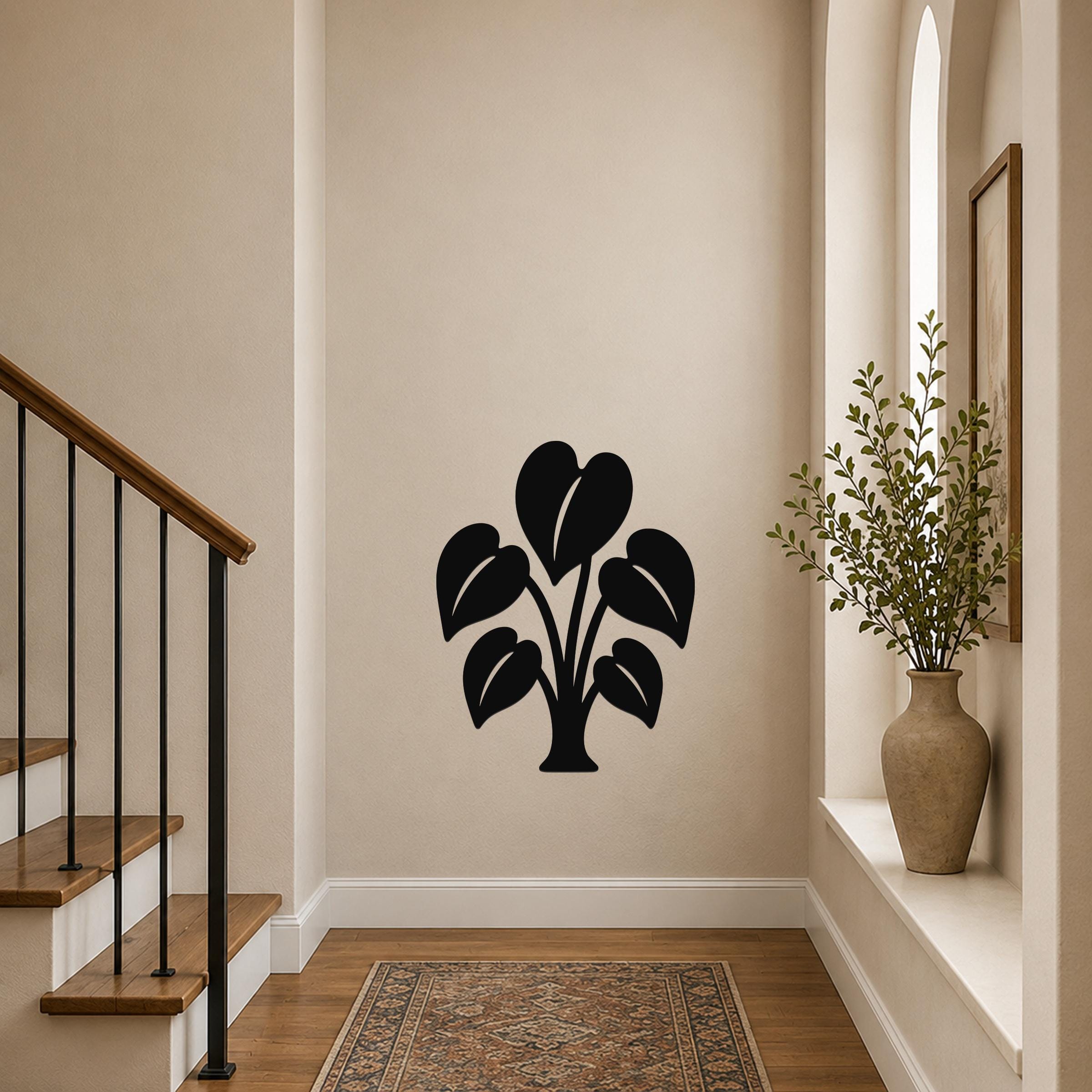 Black metal wall art in the shape of an elephant ear plant with leaf cutouts, mounted on a hallway wall above a patterned rug near a staircase.