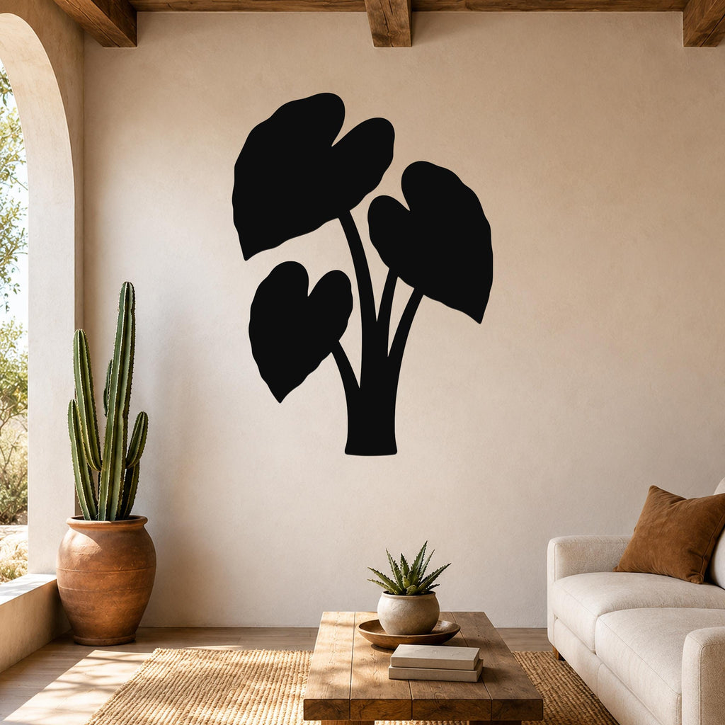 Black metal wall art silhouette of an elephant ear plant with three large leaves, mounted on a beige living room wall above a wooden coffee table.