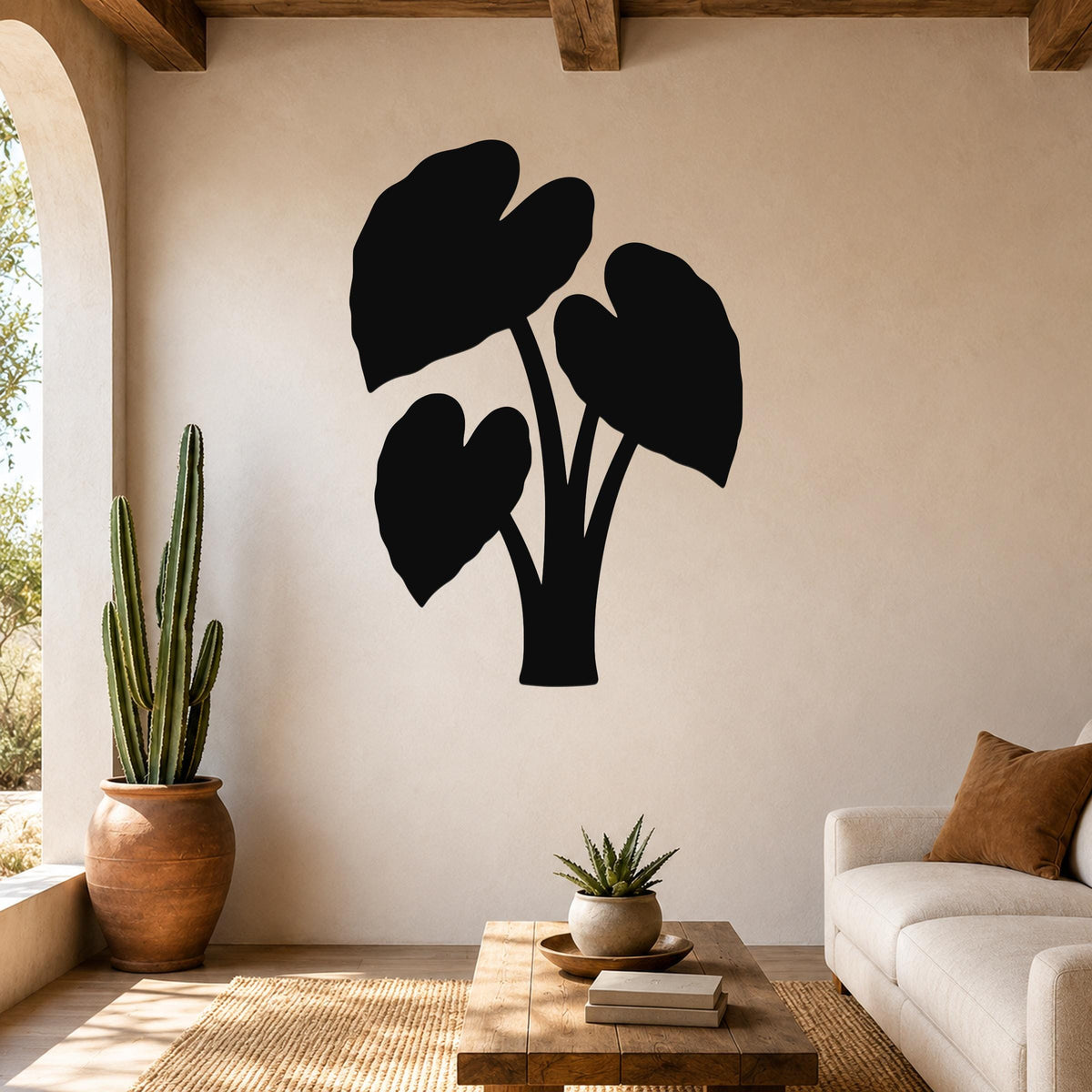 Black metal wall art silhouette of an elephant ear plant with three large leaves, mounted on a beige living room wall above a wooden coffee table.