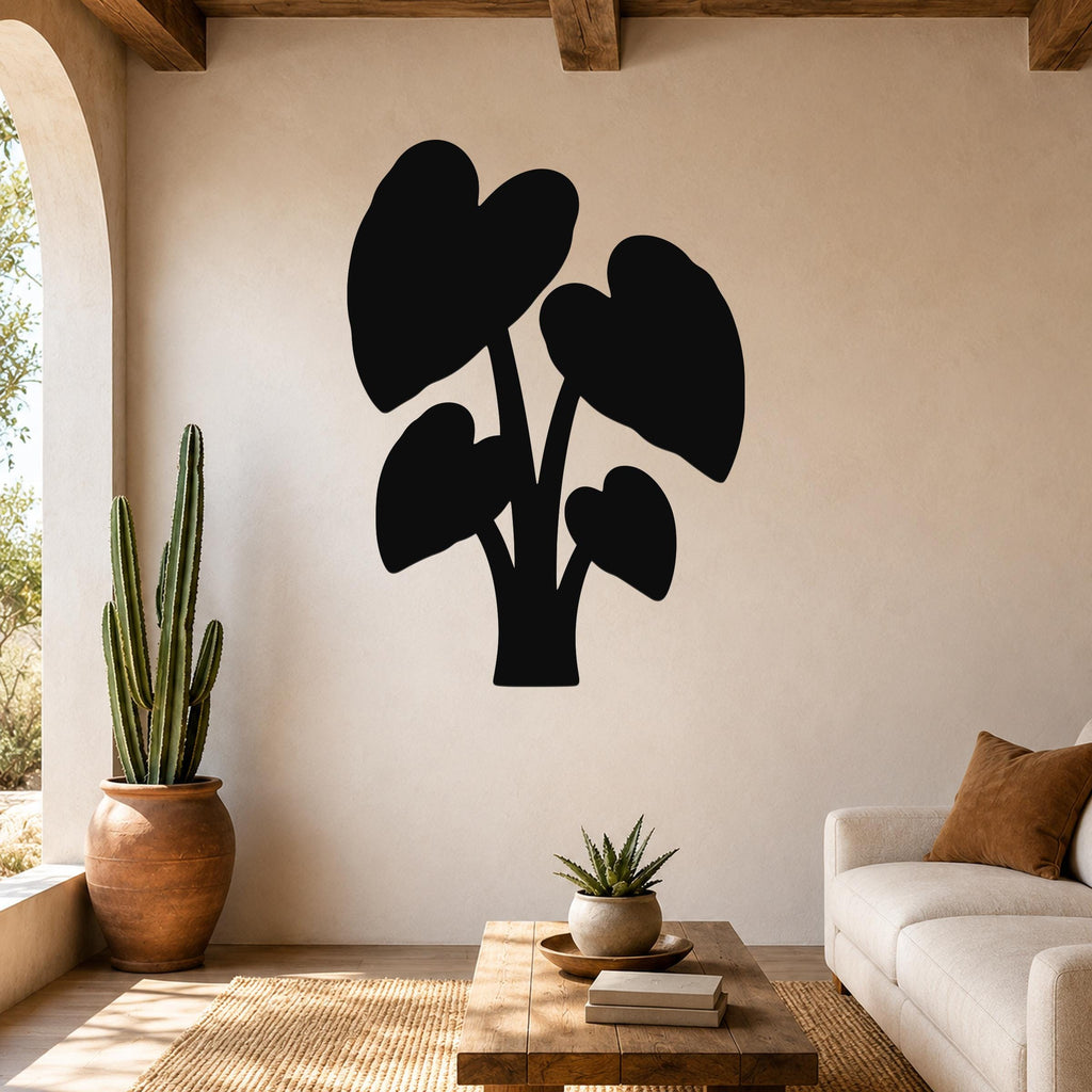 Black metal wall art silhouette of an elephant ear plant with large leaf cutouts, mounted on a living room wall above a wooden coffee table.